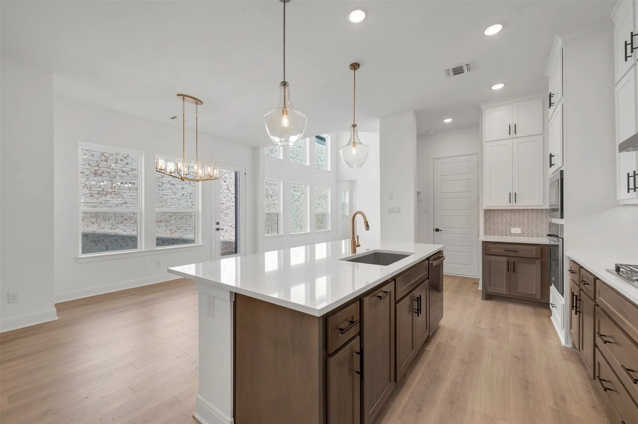 Modern kitchen with a central island featuring a sink and gold-tone faucet, white countertops, two-tone cabinetry, and wood-finish flooring