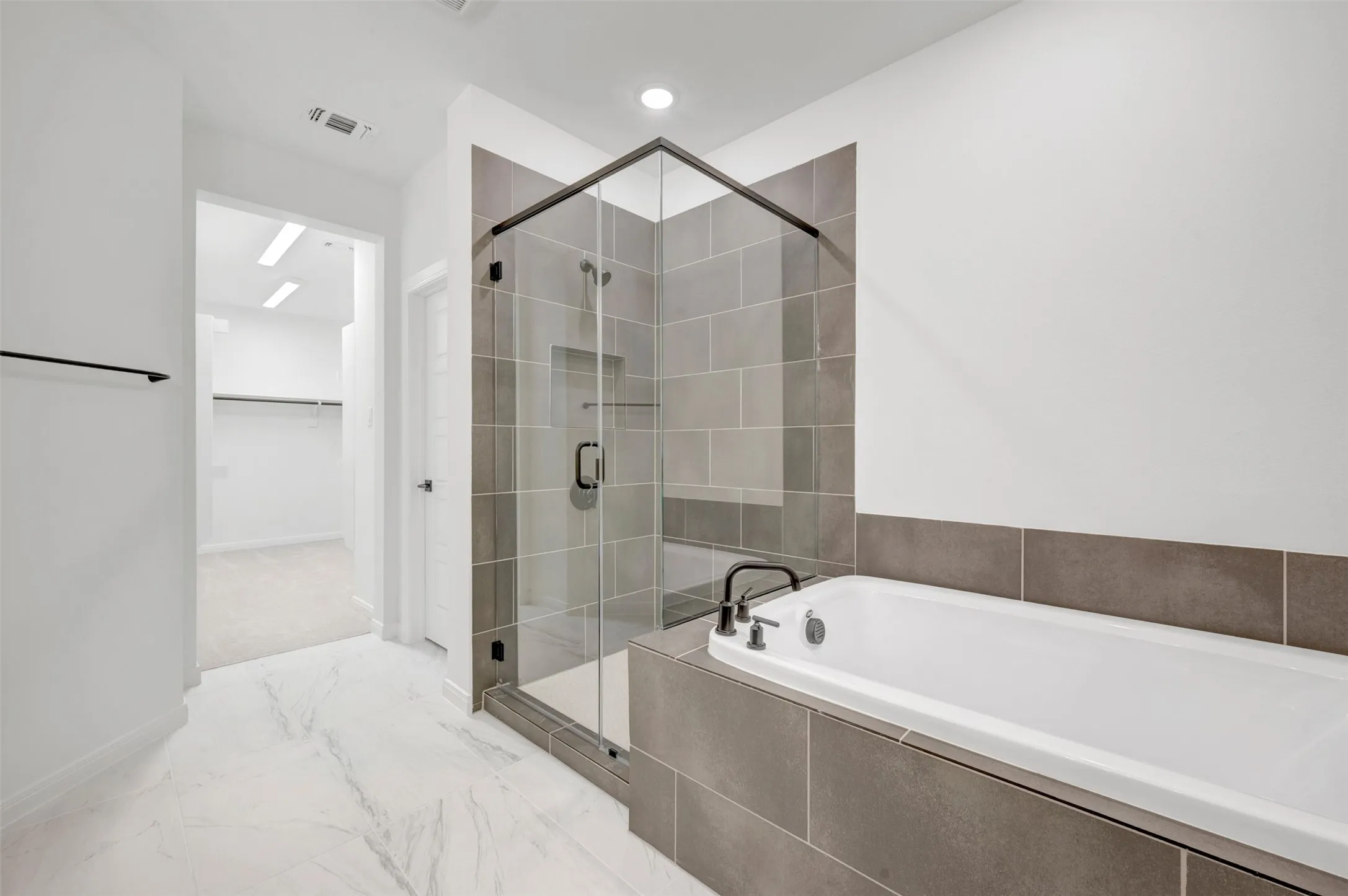 Spa-inspired primary bathroom featuring a frameless glass-enclosed shower with tile surround, freestanding soaking tub, dual vanity with integrated countertop, and recessed ceiling lighting