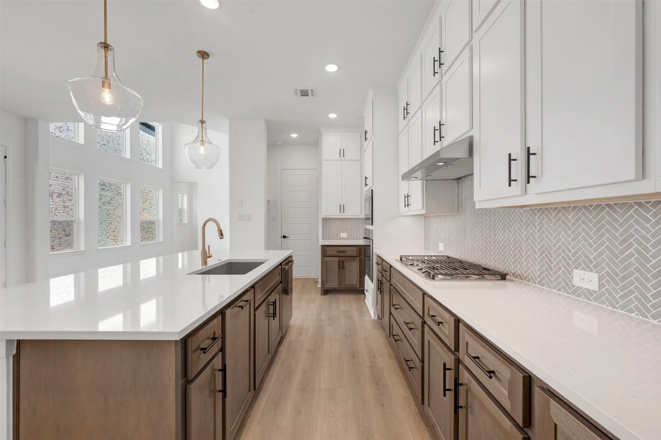 Galley kitchen featuring white cabinetry with brushed nickel hardware, white quartz countertops, herringbone tile backsplash, stainless steel gas cooktop, and wood-finish flooring throughout