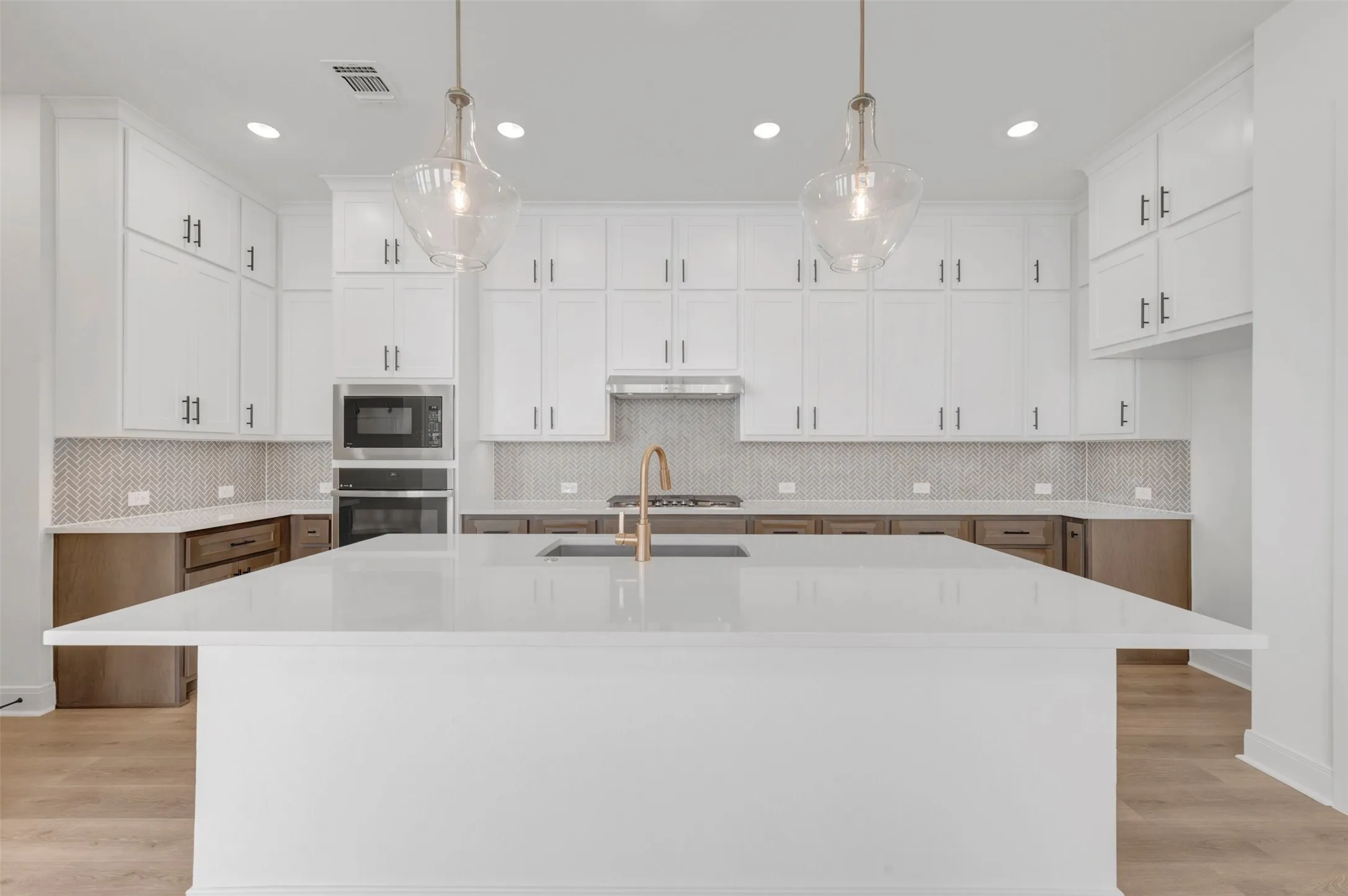 Kitchen featuring a large central island with a solid surface countertop, white upper cabinetry, wood-finish lower cabinetry, and a herringbone pattern tile backsplash