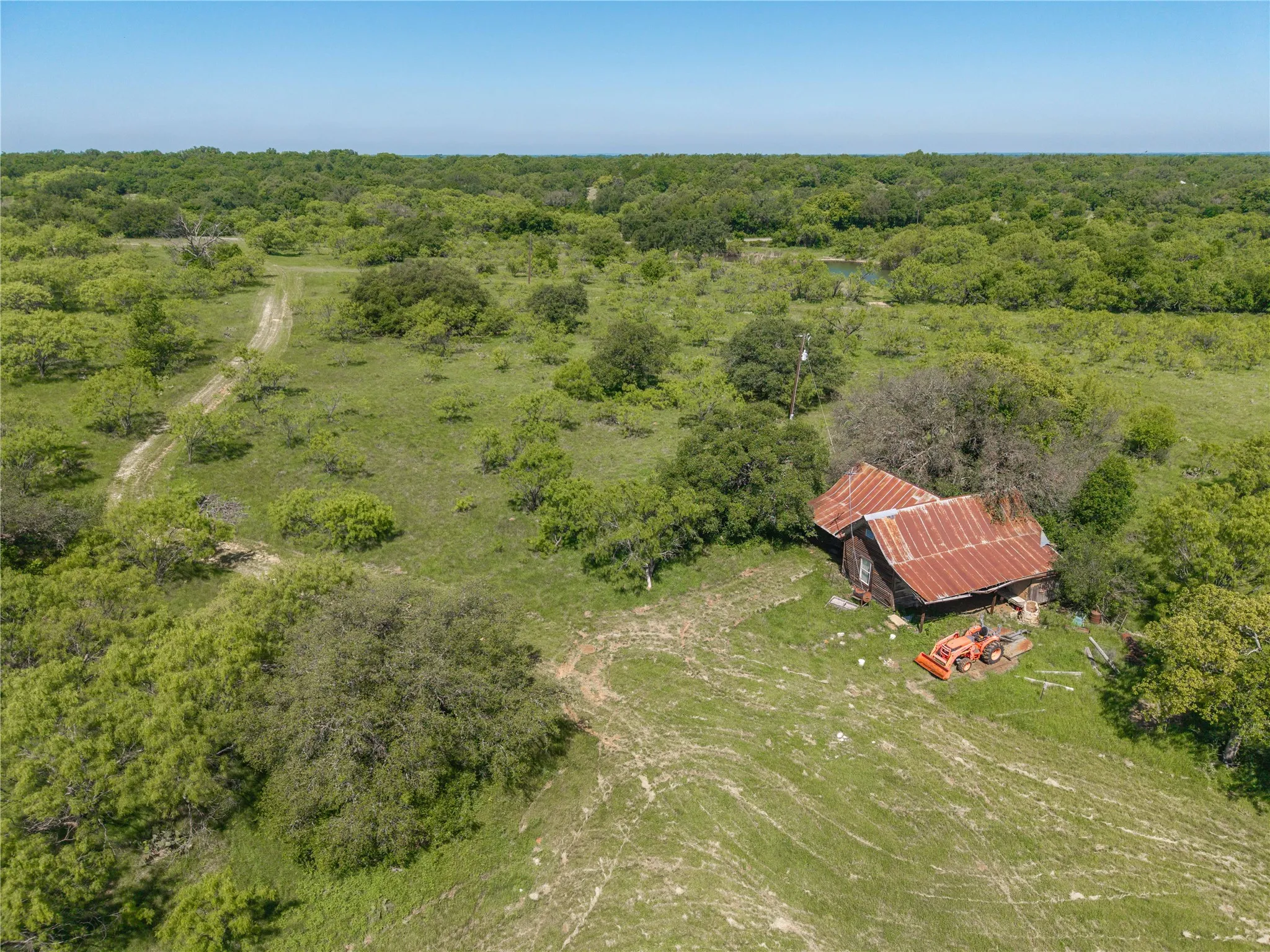 Expansive green landscape featuring mature trees and a rustic structure with a corrugated metal roof