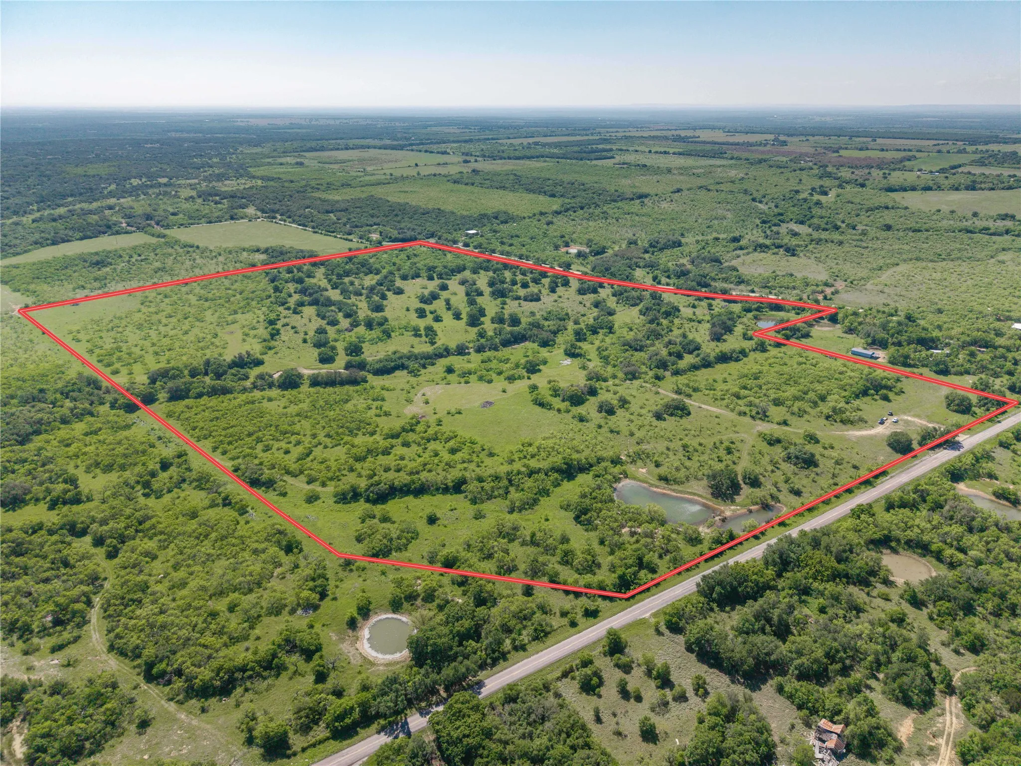 Expansive land parcel featuring natural ponds, a paved road frontage, and varied topography with mature trees and open fields