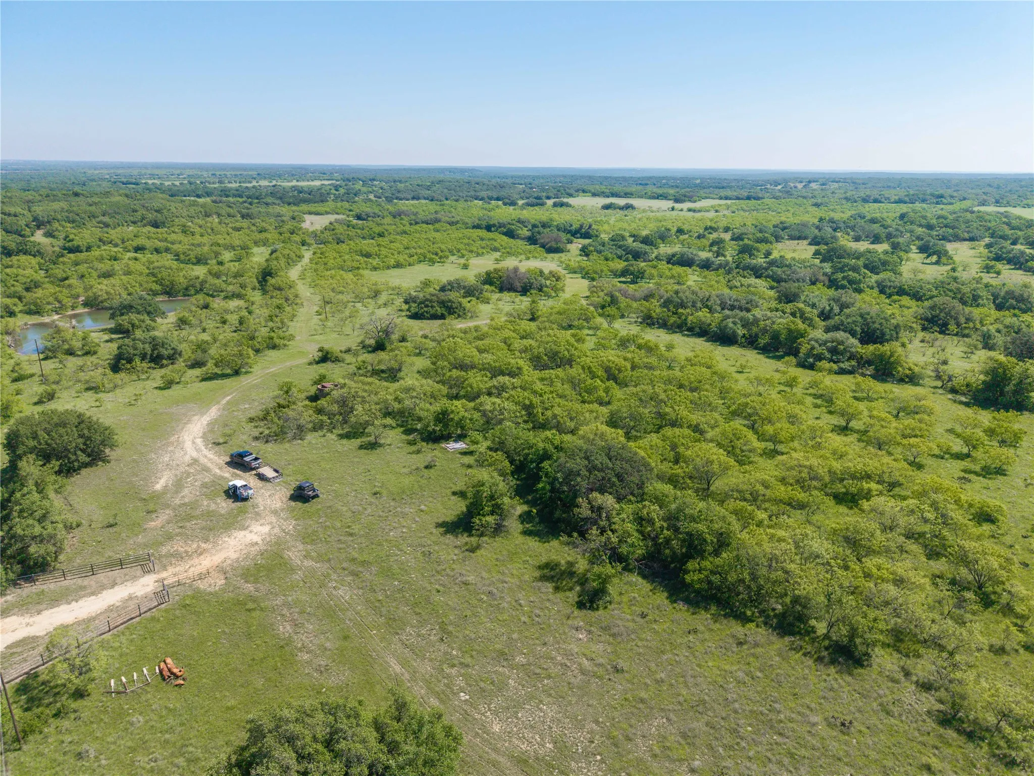 Expansive land parcel featuring a natural pond, a dirt track, and varied tree coverage