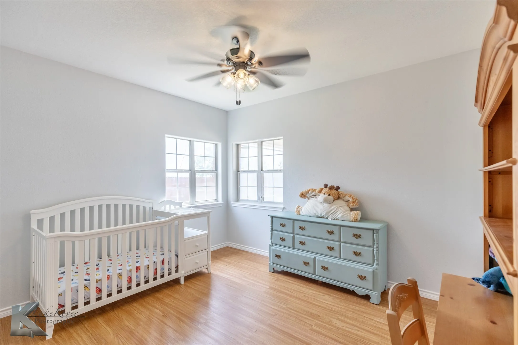 Bedroom with light wood-style floors, ceiling fan, and a nursery area