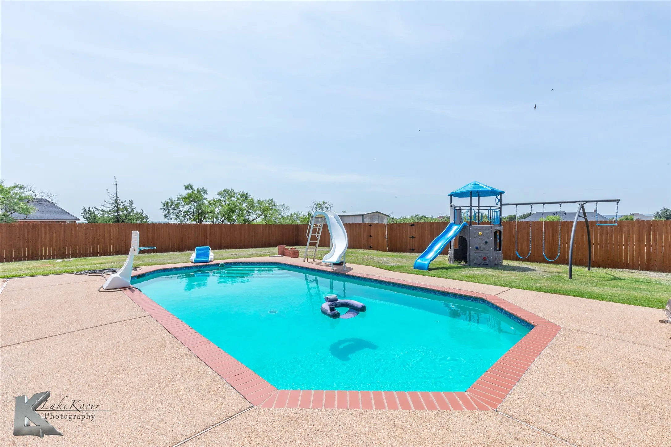 View of pool featuring a water slide, a fenced backyard, a playground, and a patio area