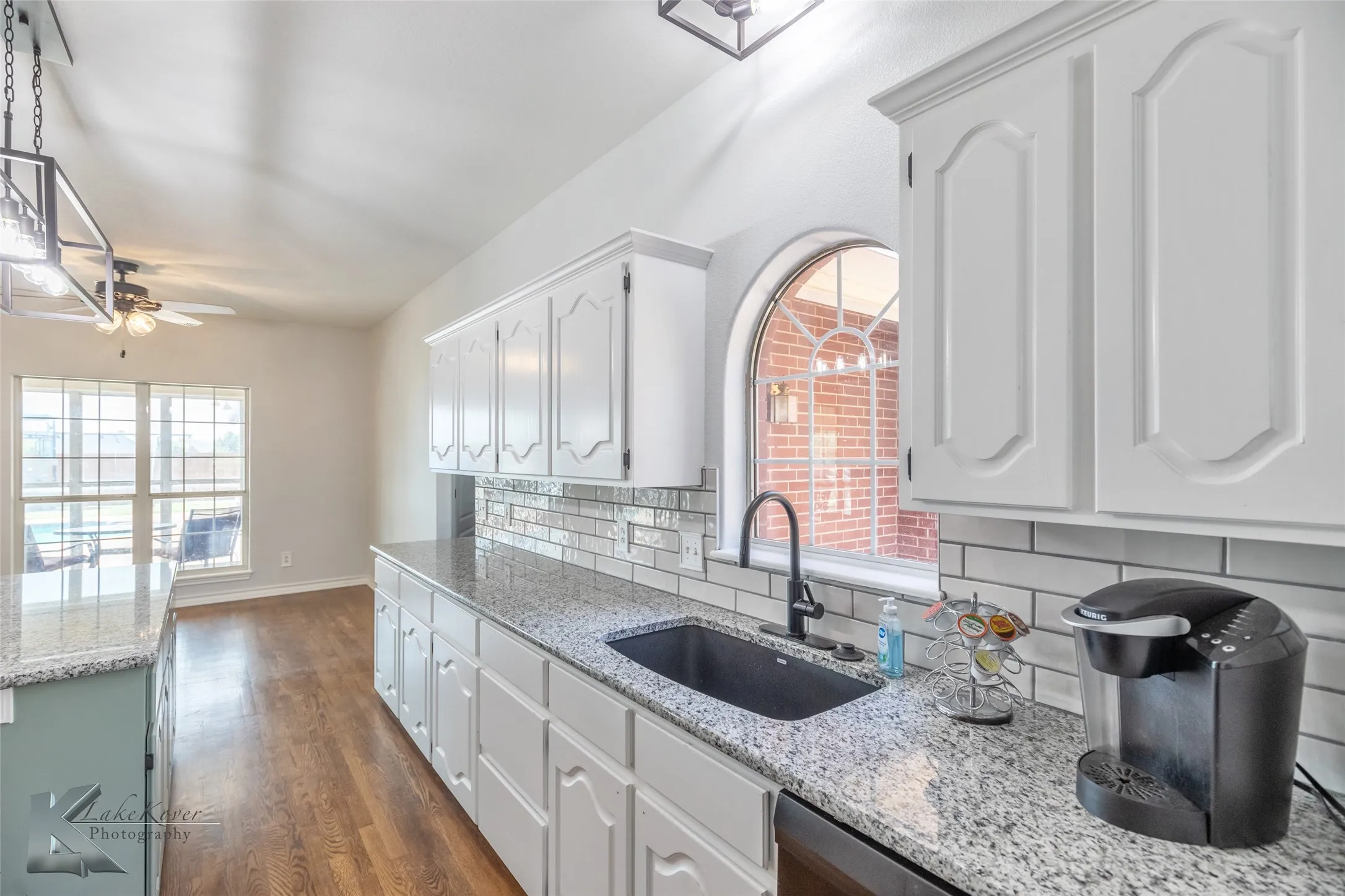 Kitchen featuring a ceiling fan, tasteful backsplash, white cabinets, dark wood finished floors, and healthy amount of natural light