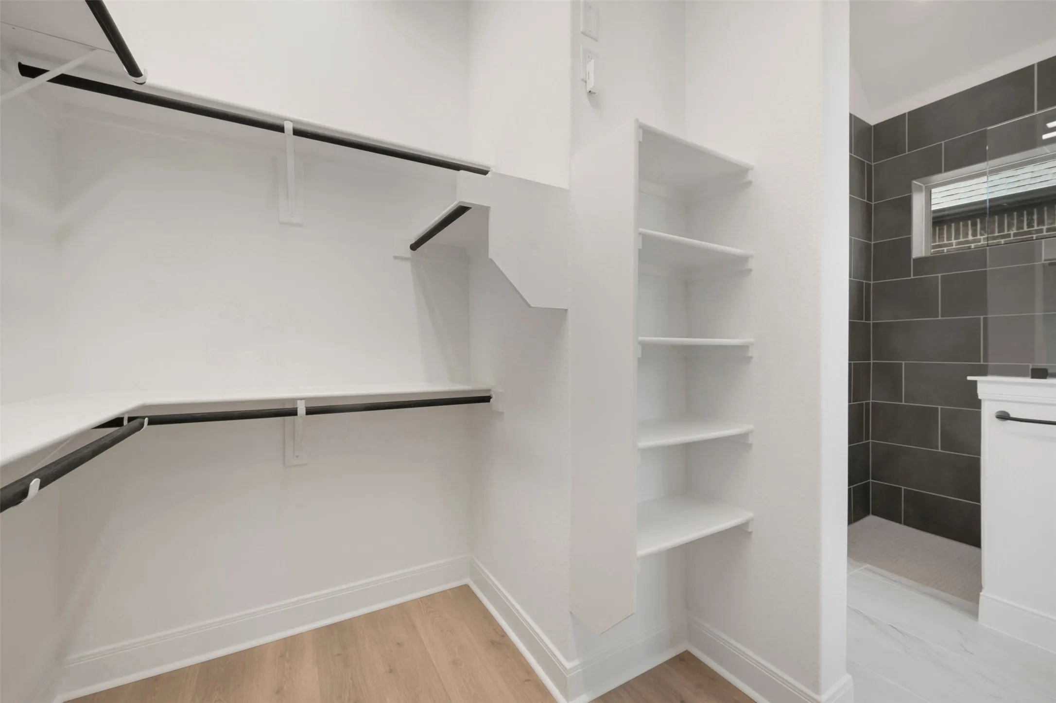 Walk-in closet with ample white shelving, black hanging rods, and wood-finish flooring