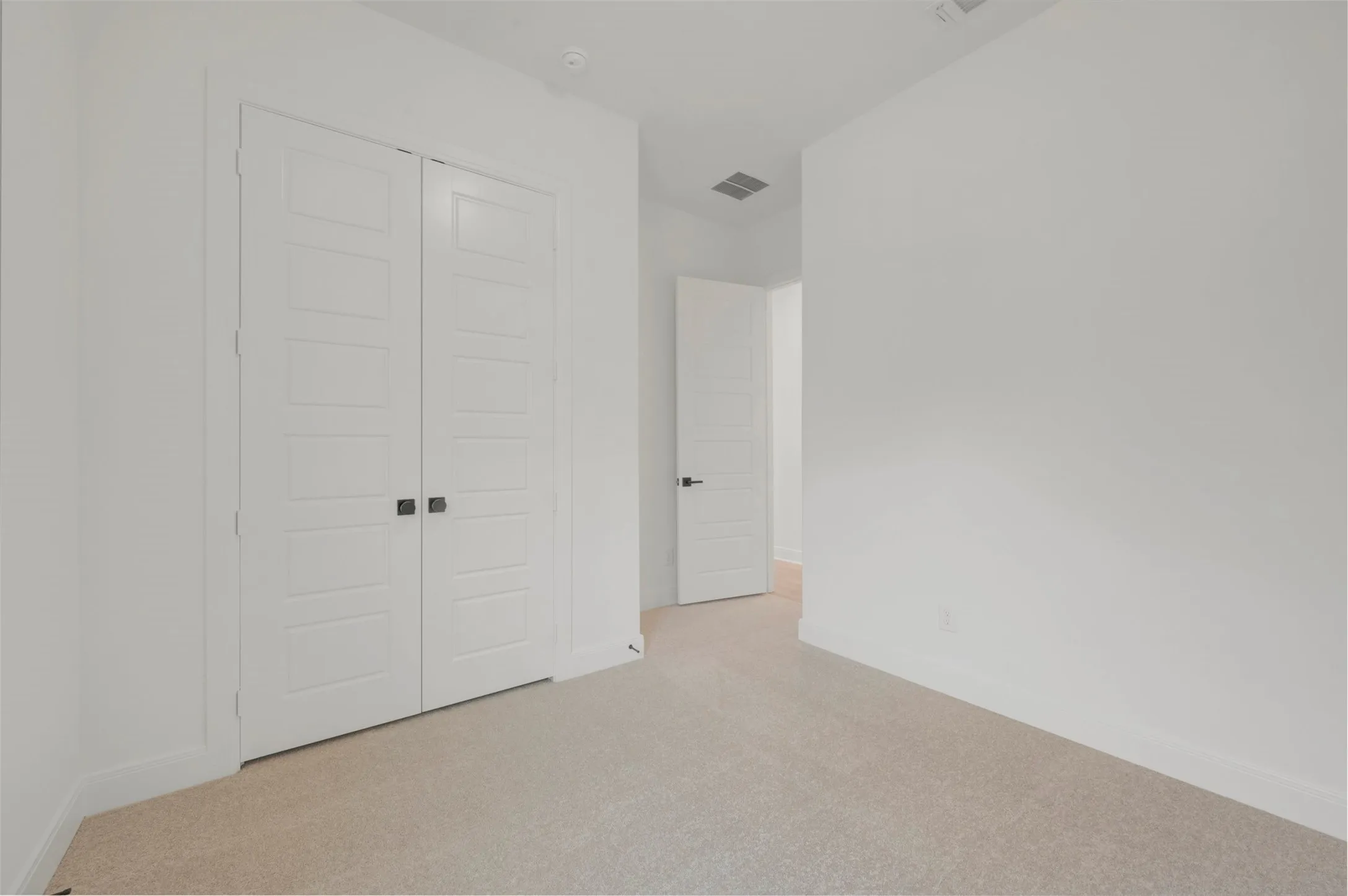 Room featuring neutral carpeting, white walls, and a pair of white paneled bifold doors with black hardware