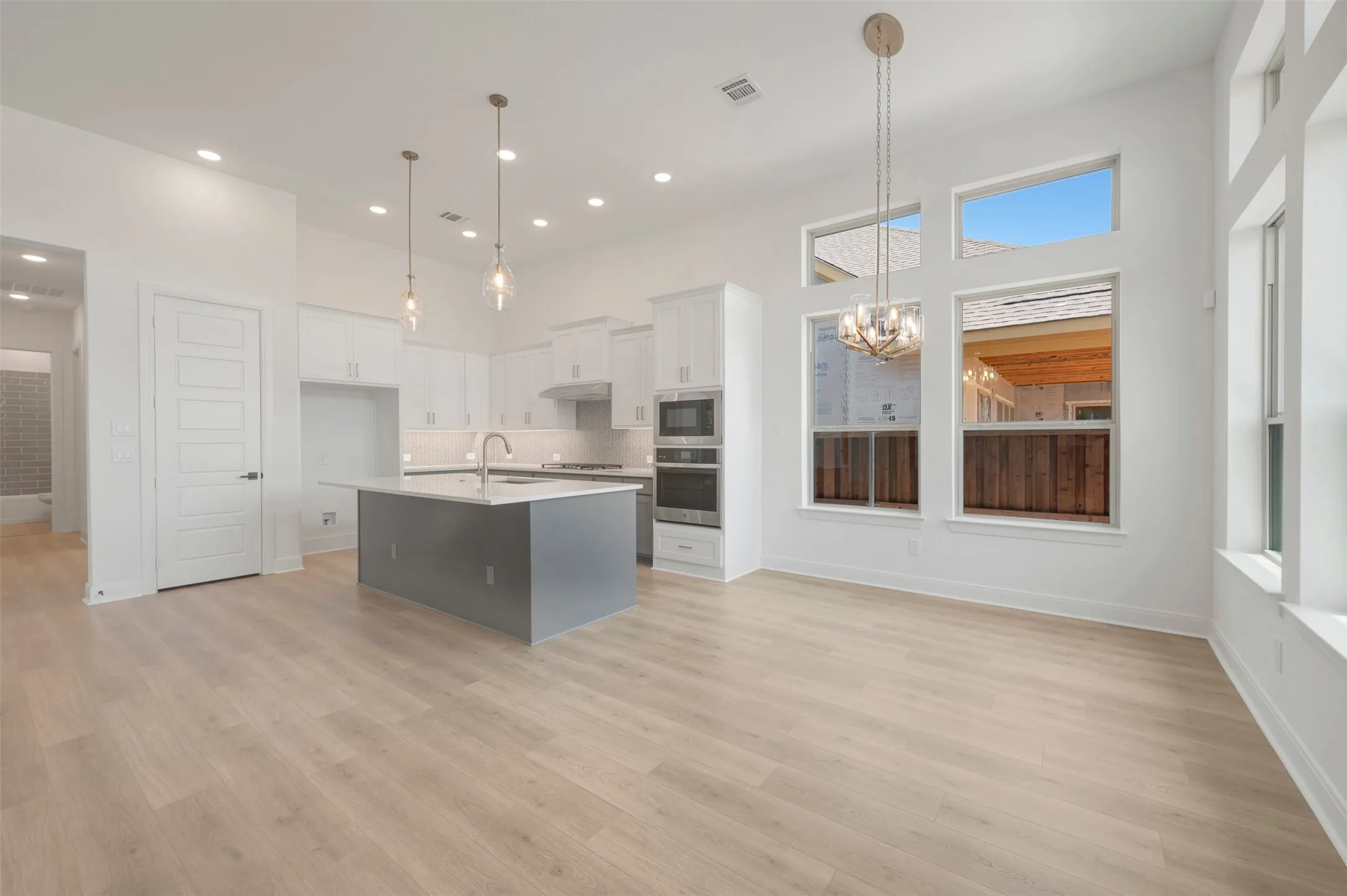 Open-concept living space featuring wood-finish flooring, a contemporary kitchen island with a sink, white cabinetry, and stainless steel appliances