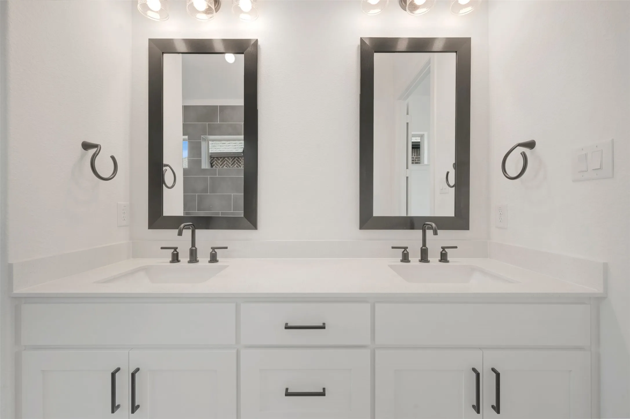 Dual vanity with white cabinetry, integrated sinks, dark bronze hardware, and framed mirrors