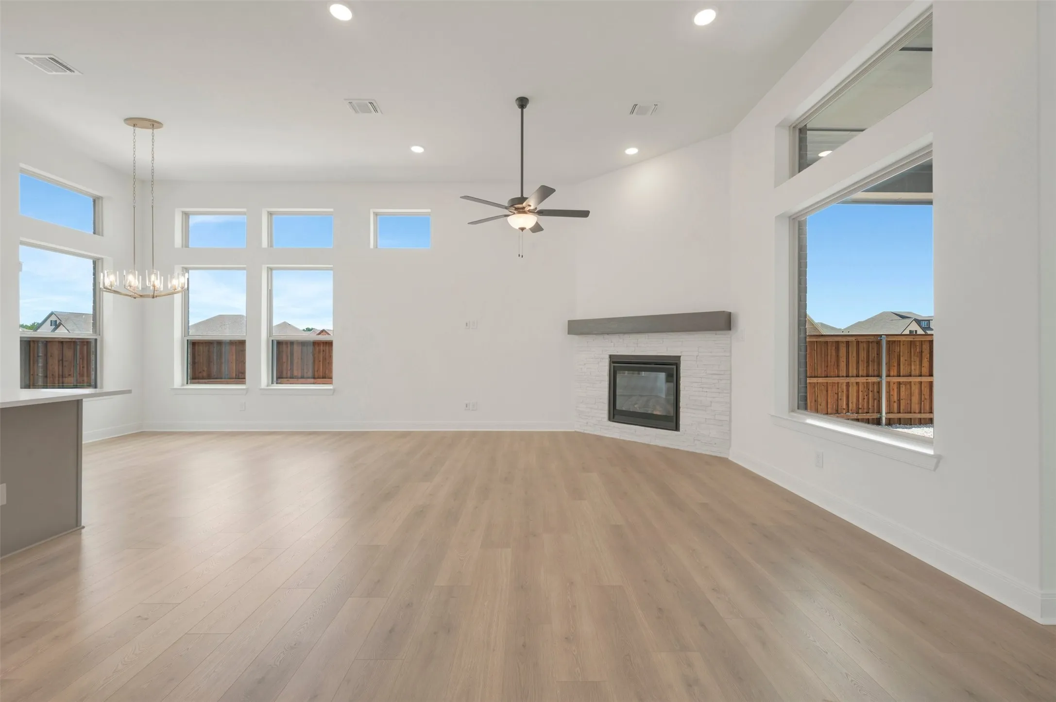 Bright living area featuring wood-finish flooring, a modern fireplace with a white tile surround, a dark wood mantle, and an abundance of natural light from multiple windows
