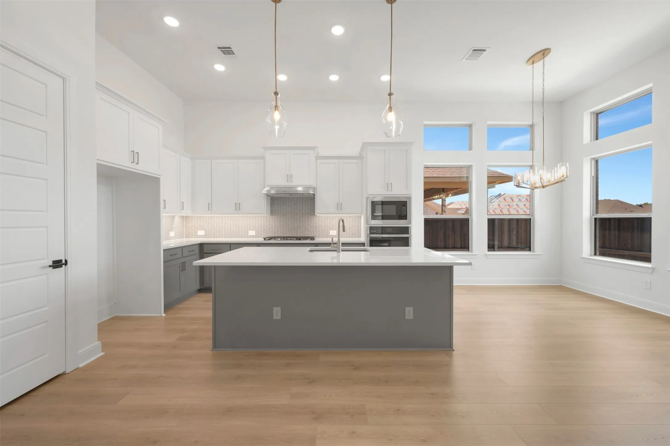 Spacious kitchen and dining area featuring light wood-finish flooring, a large central island with a sink, stainless steel appliances, and abundant natural light from multiple windows