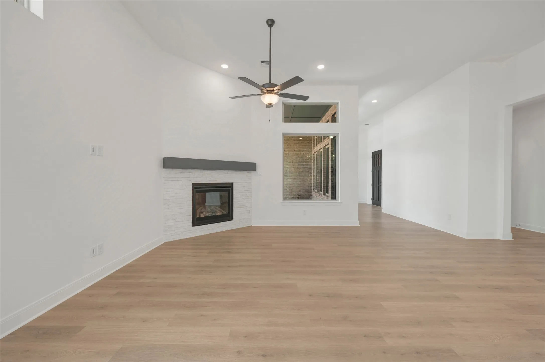 Spacious interior featuring wood-finish flooring, a white brick fireplace with a dark mantel, a ceiling fan, and recessed lighting