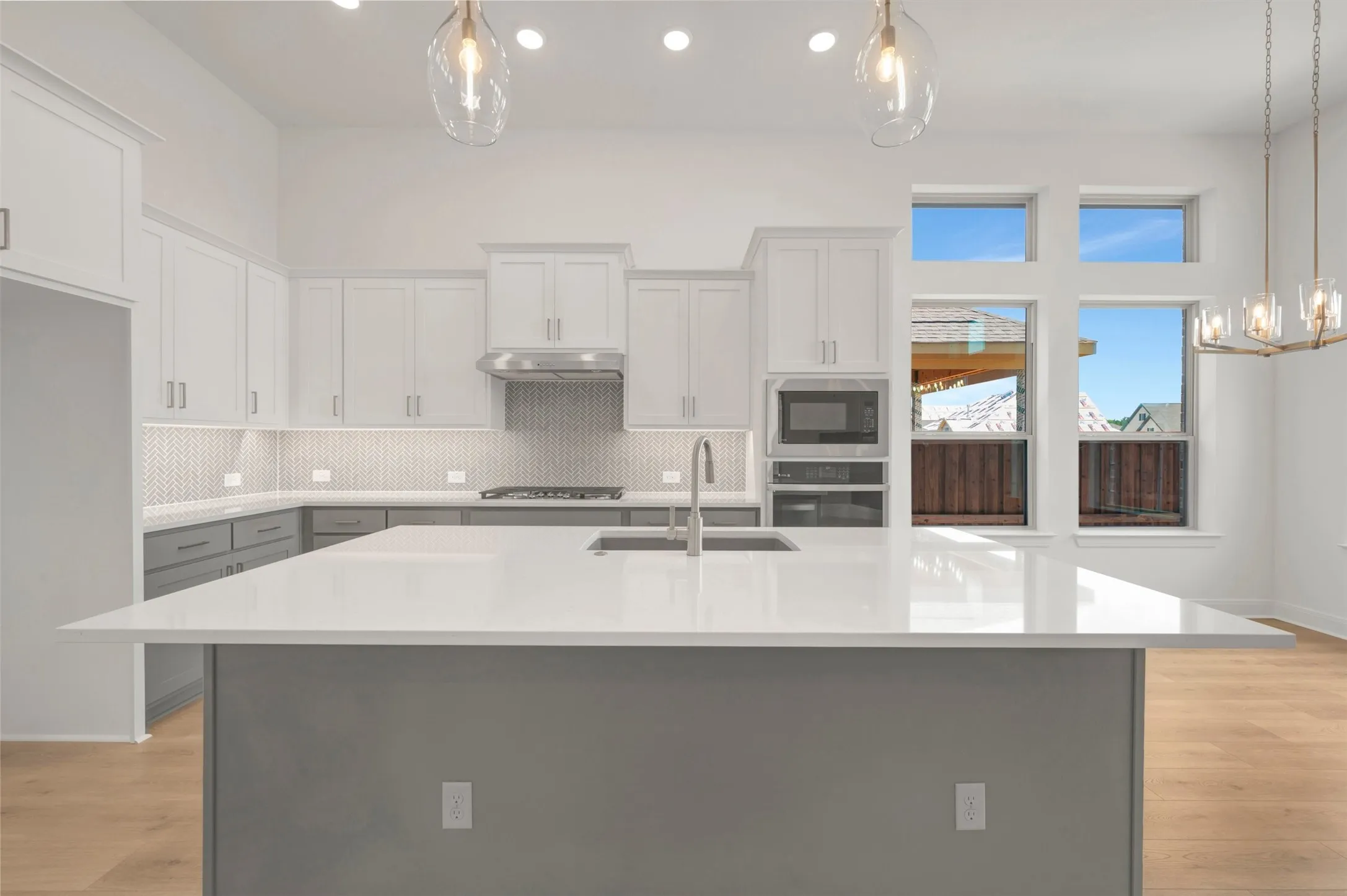 Kitchen featuring a large central island with a solid surface countertop, white upper cabinetry, gray lower cabinetry, stainless steel appliances, and a mosaic tile backsplash