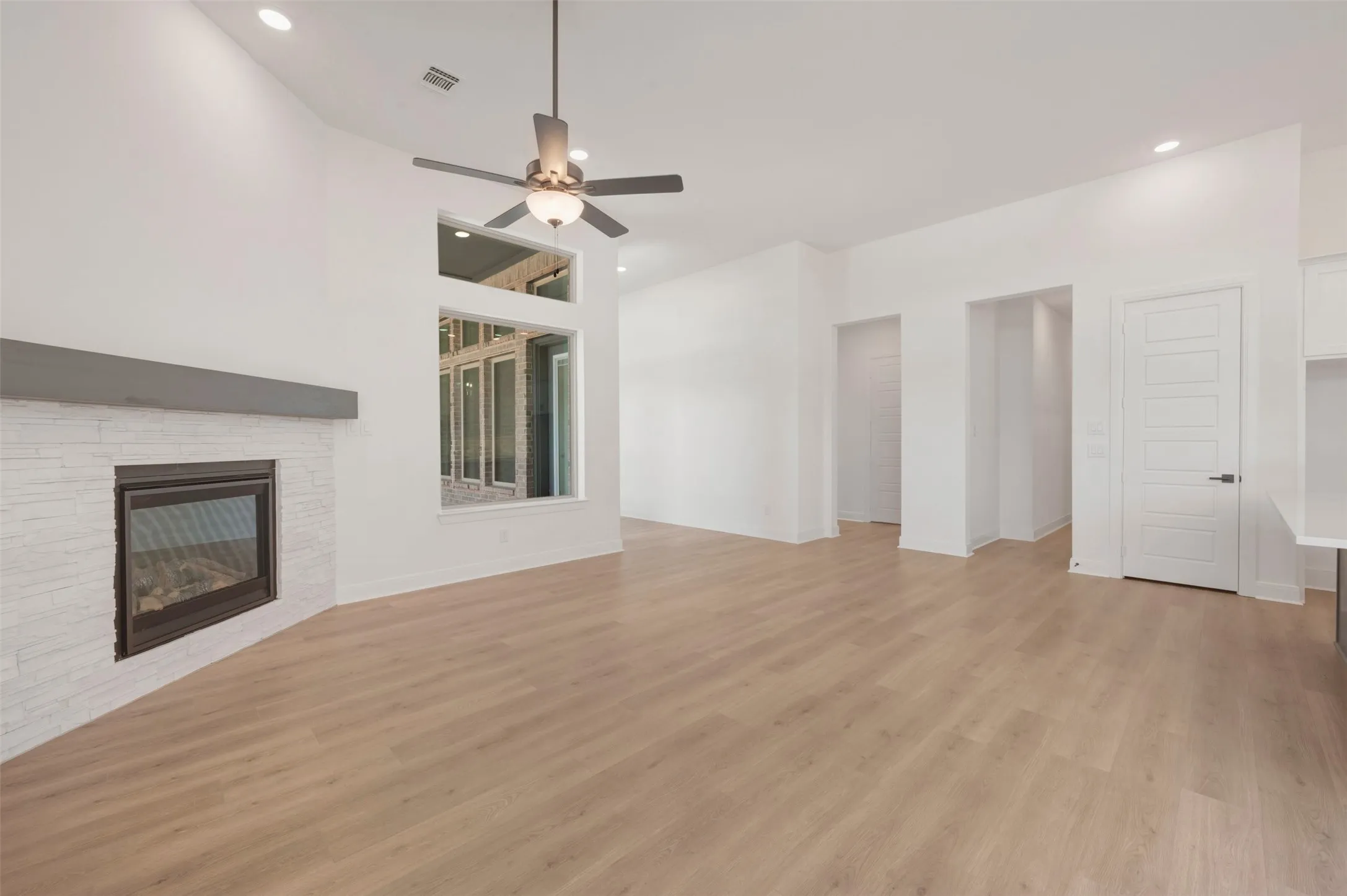 Spacious living area featuring high vaulted ceilings, light wood-finish flooring, and a modern fireplace with a white brick surround and dark mantel