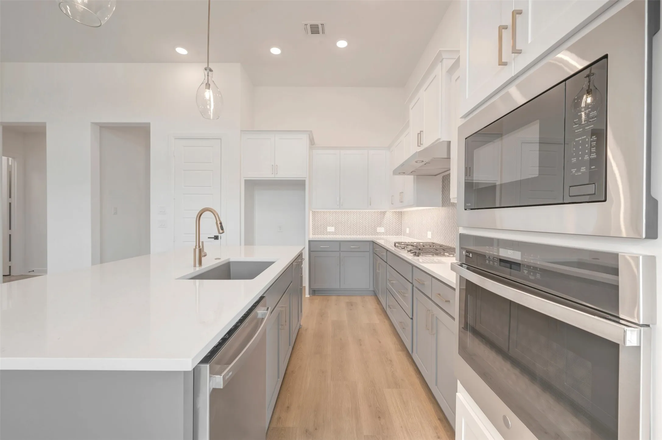 Modern kitchen featuring an expansive island with an undermount sink, a gold-finish faucet, and integrated stainless steel appliances
