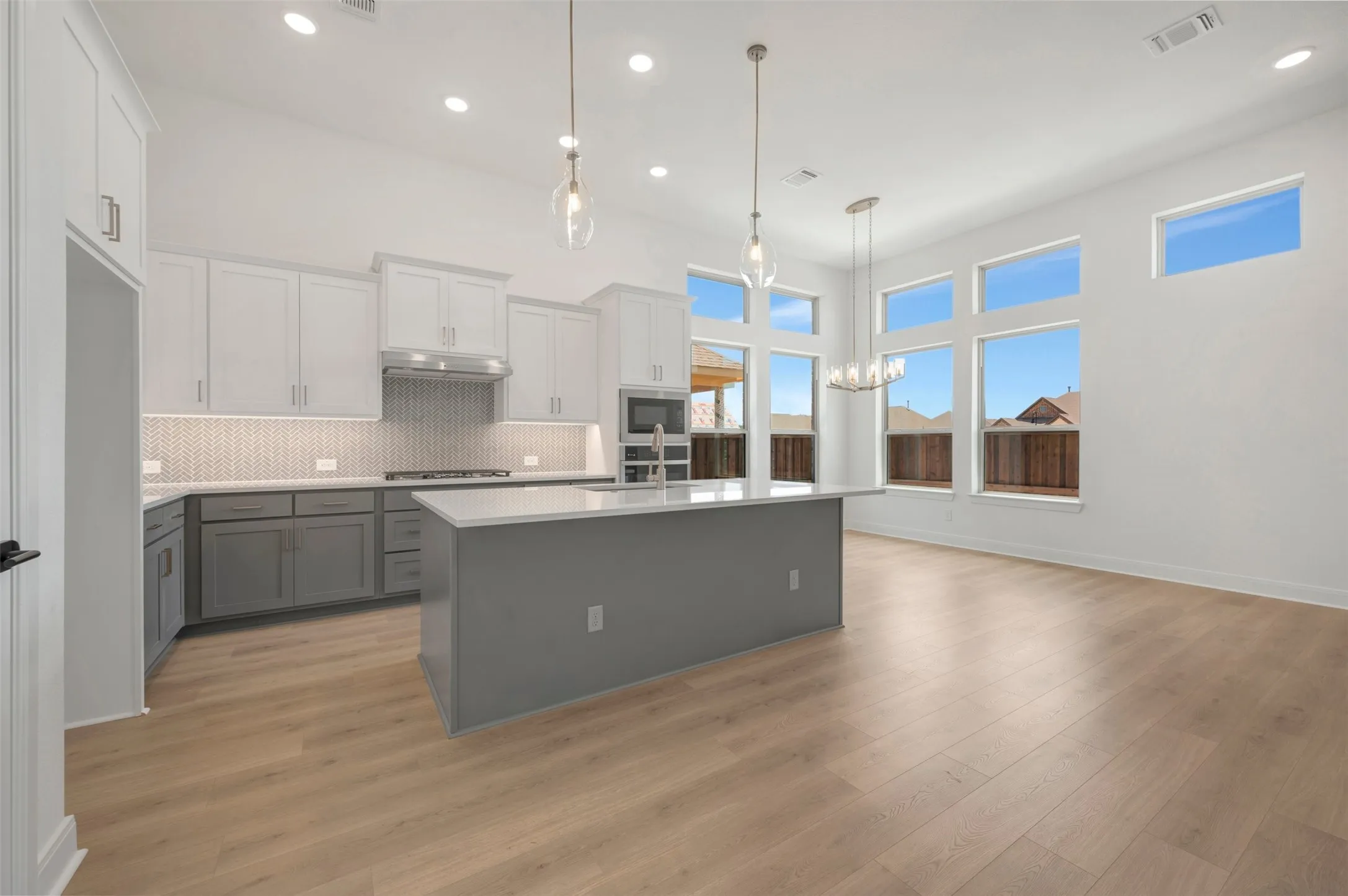 Open-concept kitchen and living area featuring wood-finish flooring, a two-tone cabinetry system, an eat-at island, and a full suite of windows