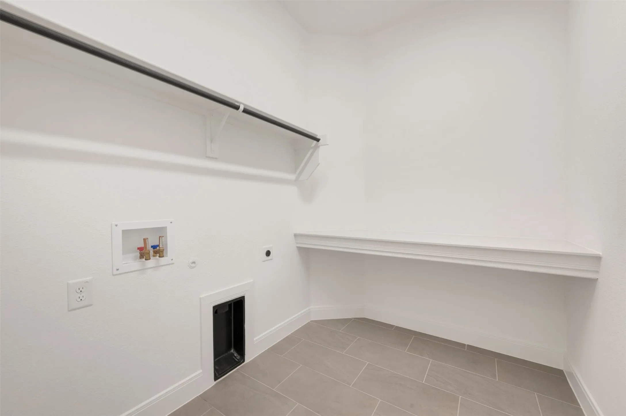 Dedicated utility space featuring tiled flooring, a built-in hanging rod, a wall-mounted shelf, and appliance hookups