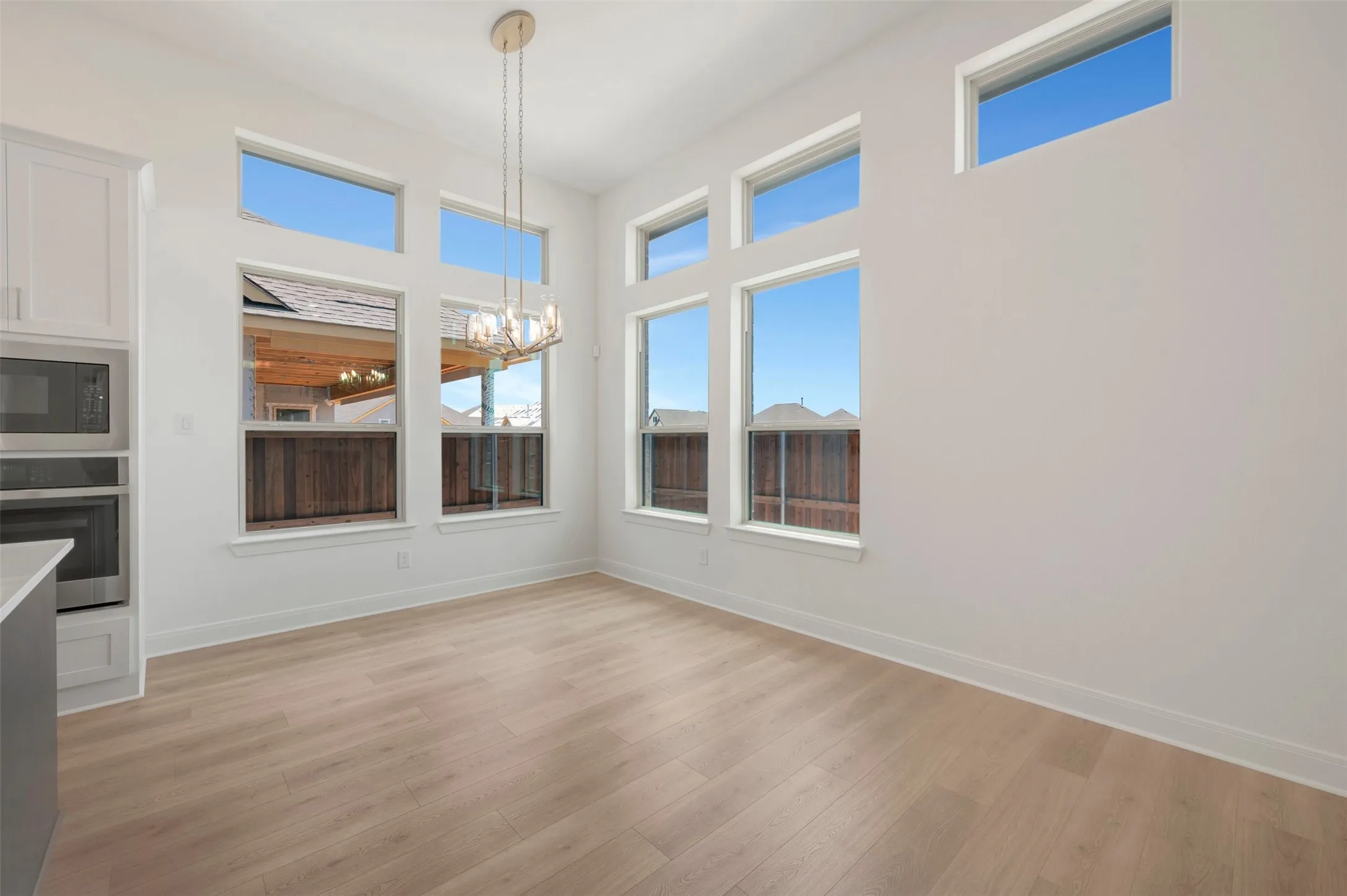 Bright interior space featuring light wood-finish flooring, numerous windows, and a contemporary chandelier