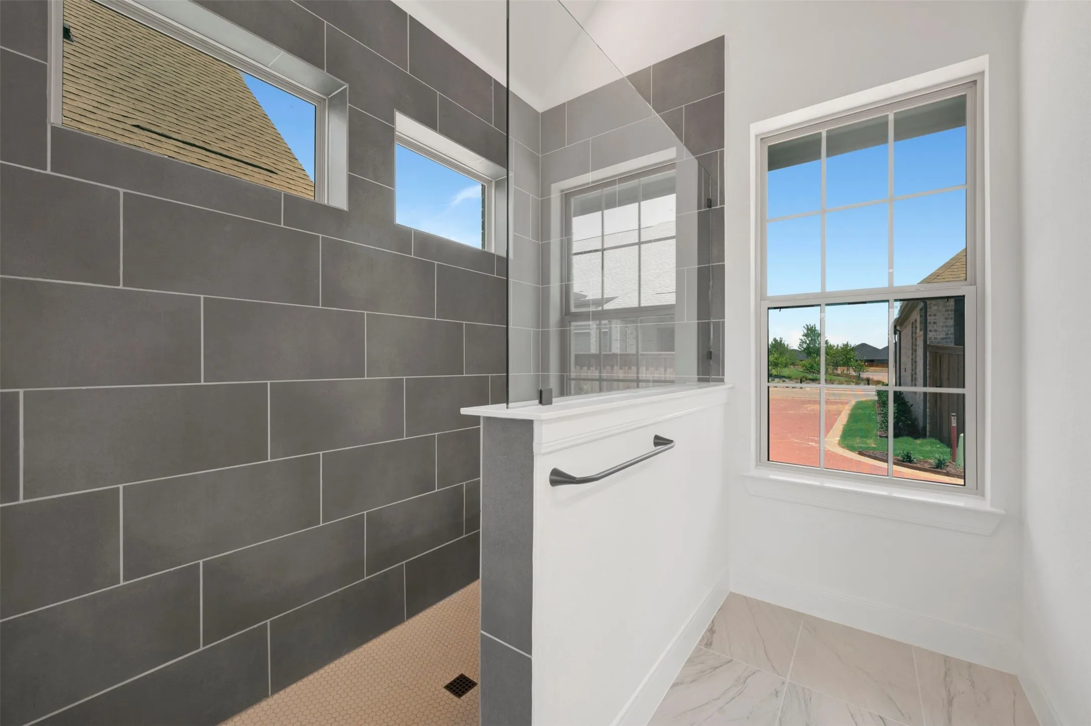 Shower enclosure featuring dark gray rectangular wall tiling, a clear glass partition, and a matte black towel bar