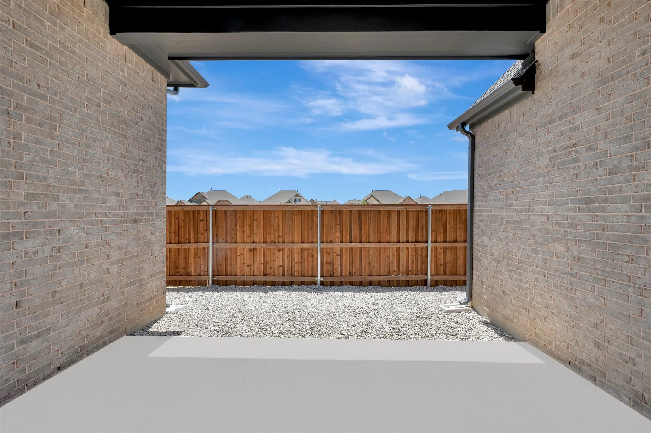 Outdoor patio area featuring a concrete slab, gravel, and a wood fence