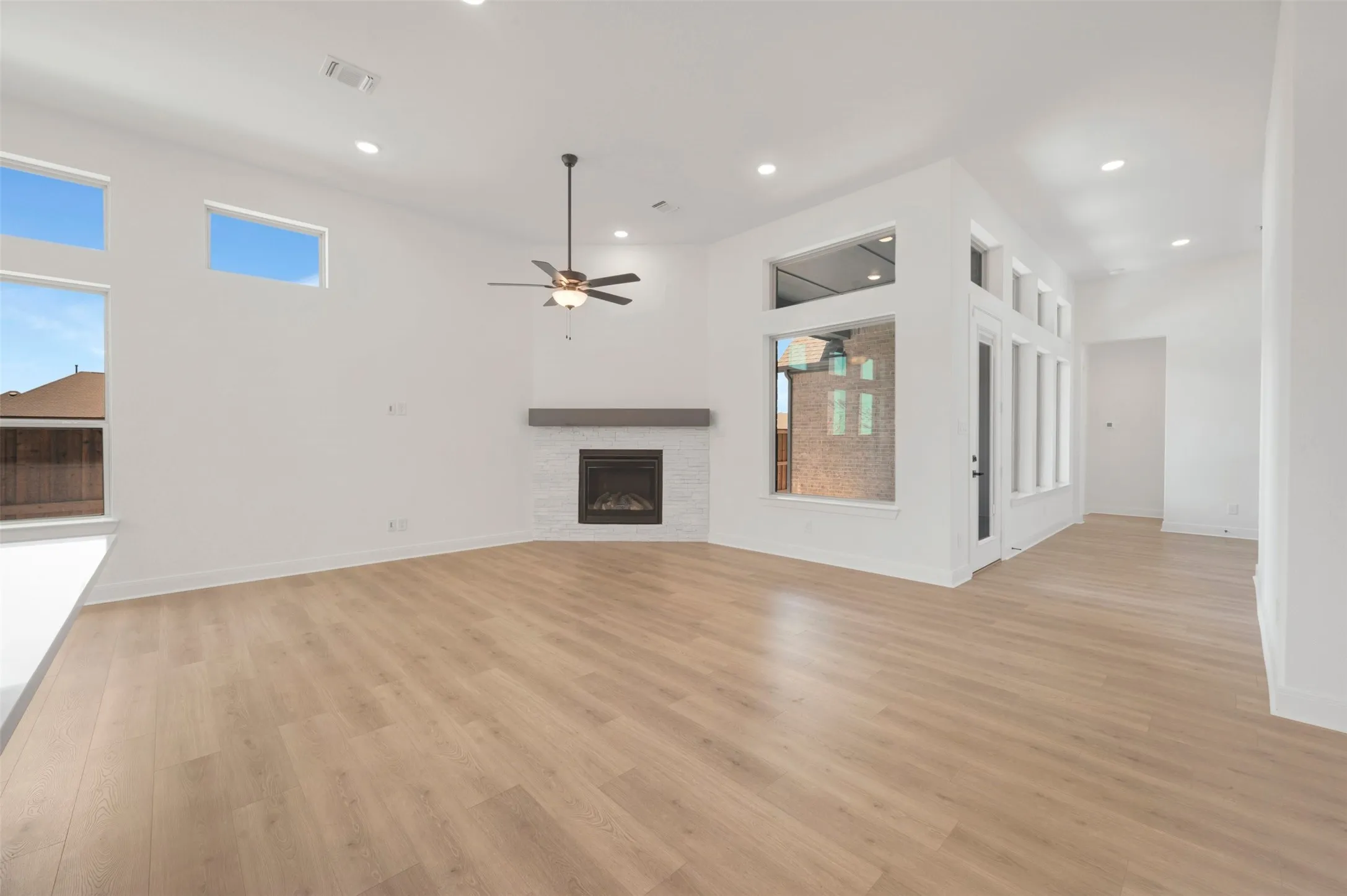 Spacious room featuring wood-finish flooring, a corner fireplace with a white tile surround and wood mantel, and a ceiling fan