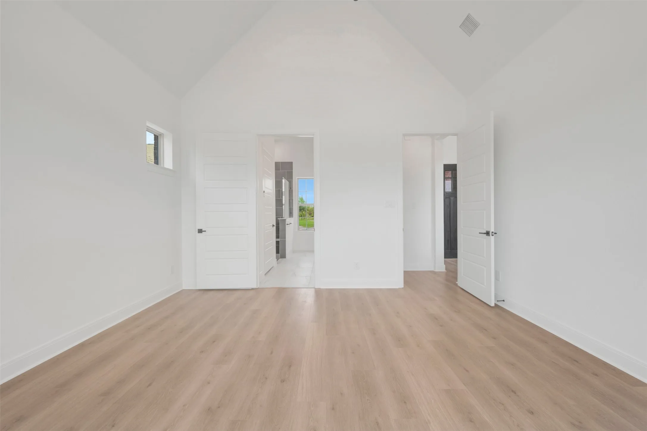 Vaulted ceiling room featuring light wood-finish flooring, white walls, and a transom window