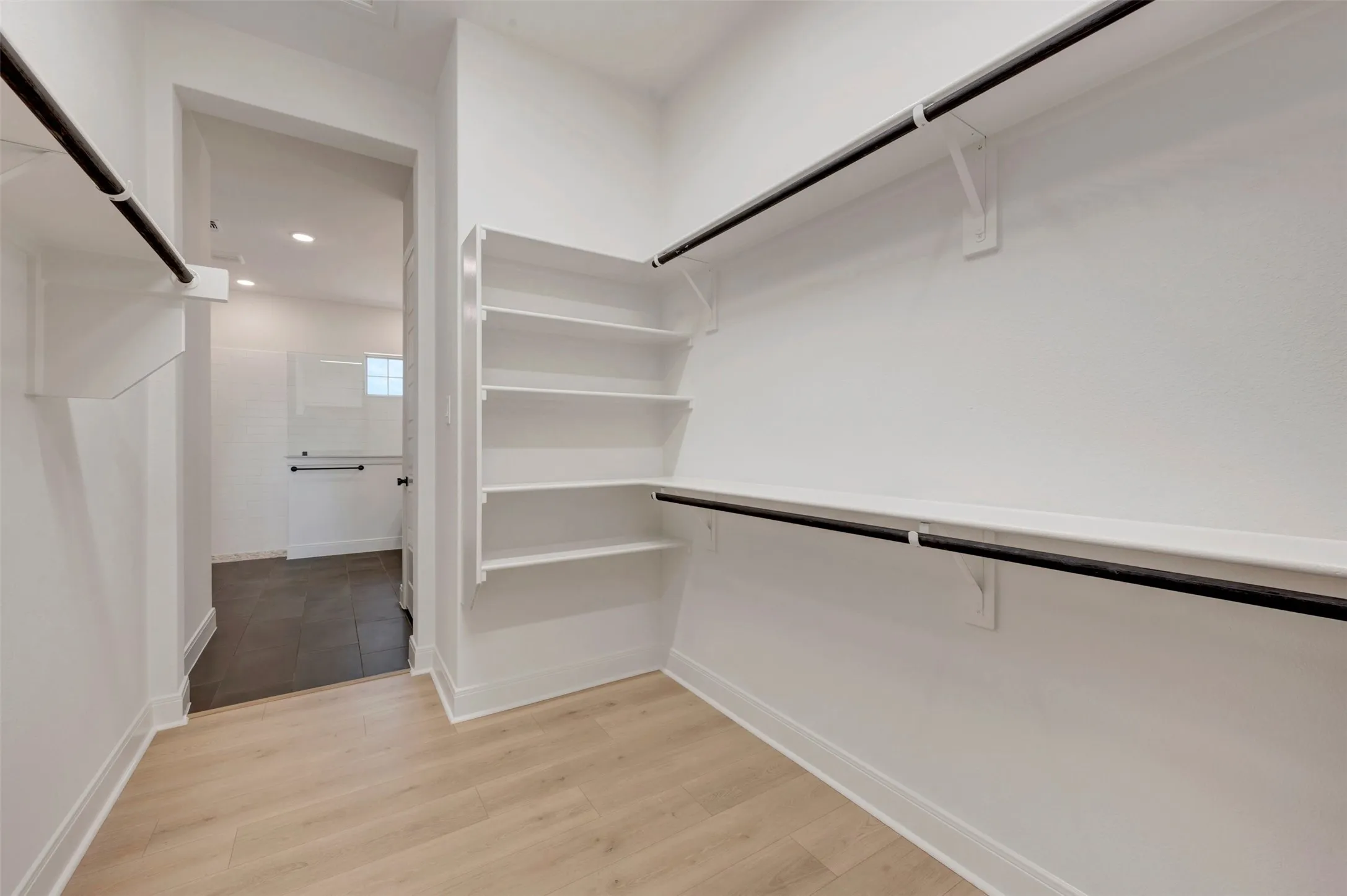 Walk-in closet featuring light wood-finish flooring, white walls, and built-in shelving