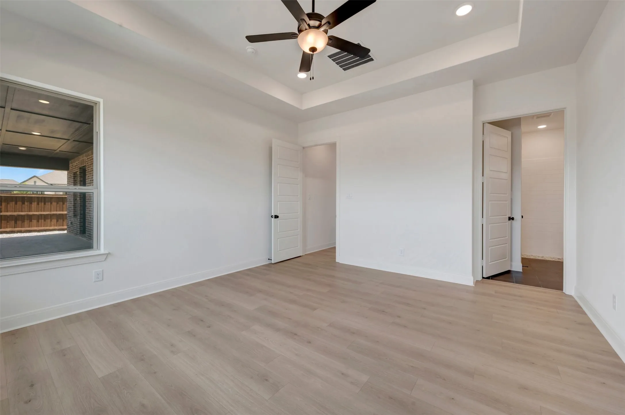 Spacious room featuring light wood-finish flooring, a contemporary ceiling fan, and a tray ceiling