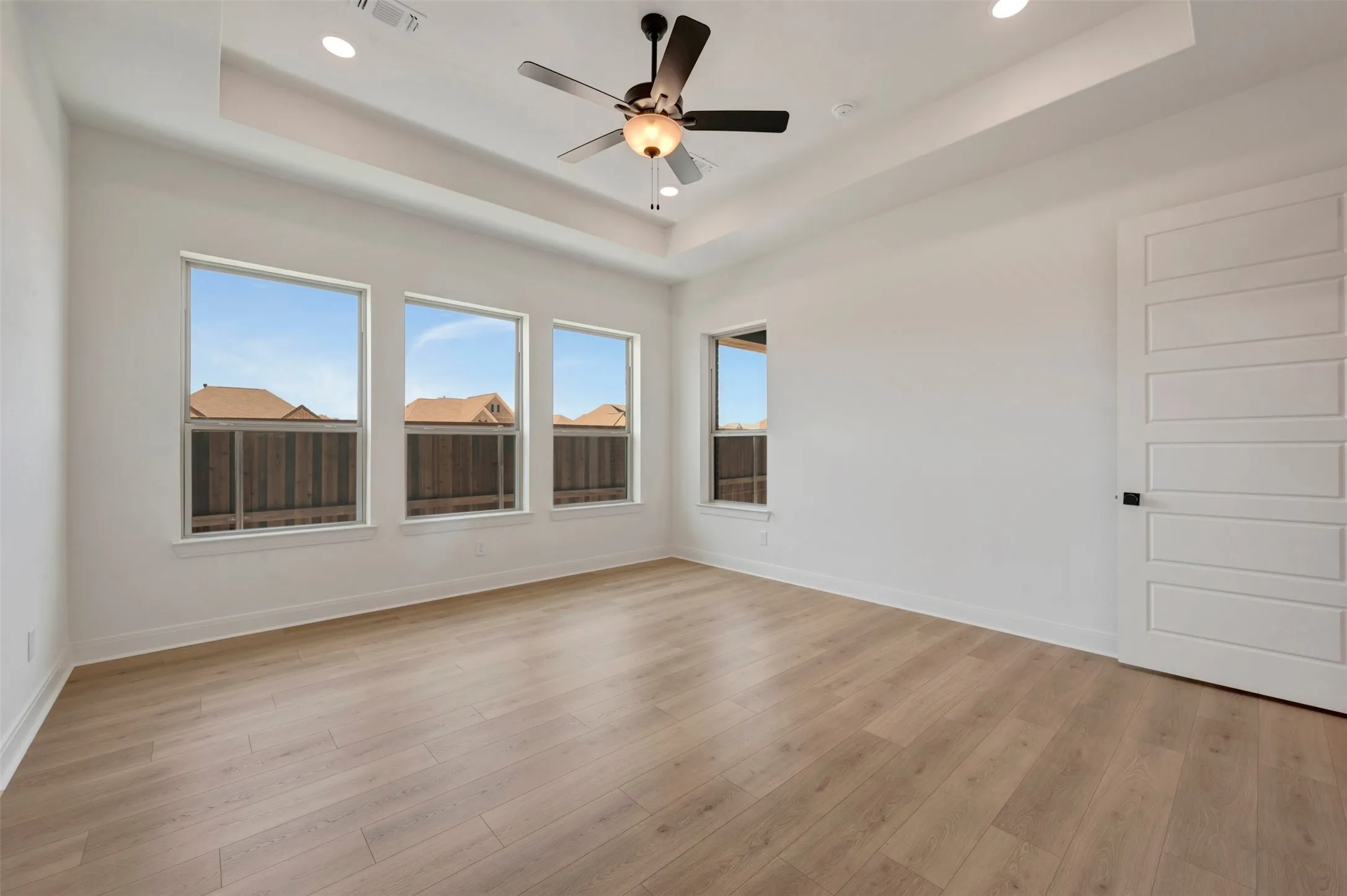 Spacious room featuring light wood-finish flooring and a tray ceiling with recessed lighting
