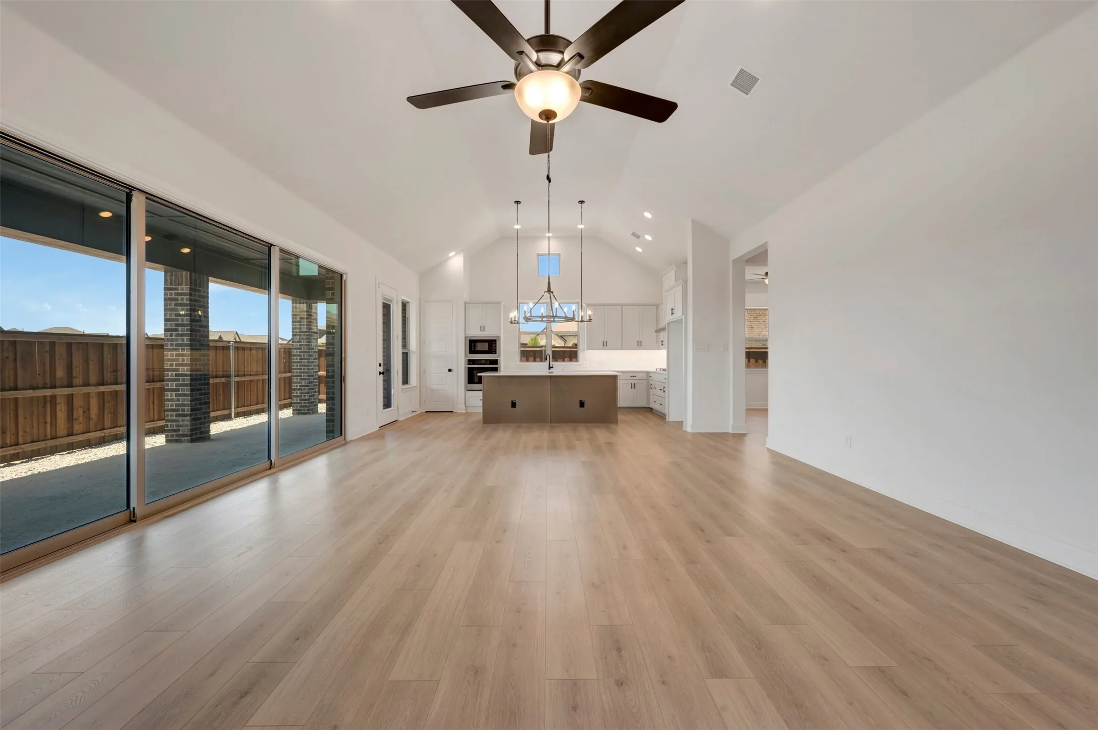 Spacious open-concept living area featuring wood-finish flooring, vaulted ceiling, and an integrated ceiling fan