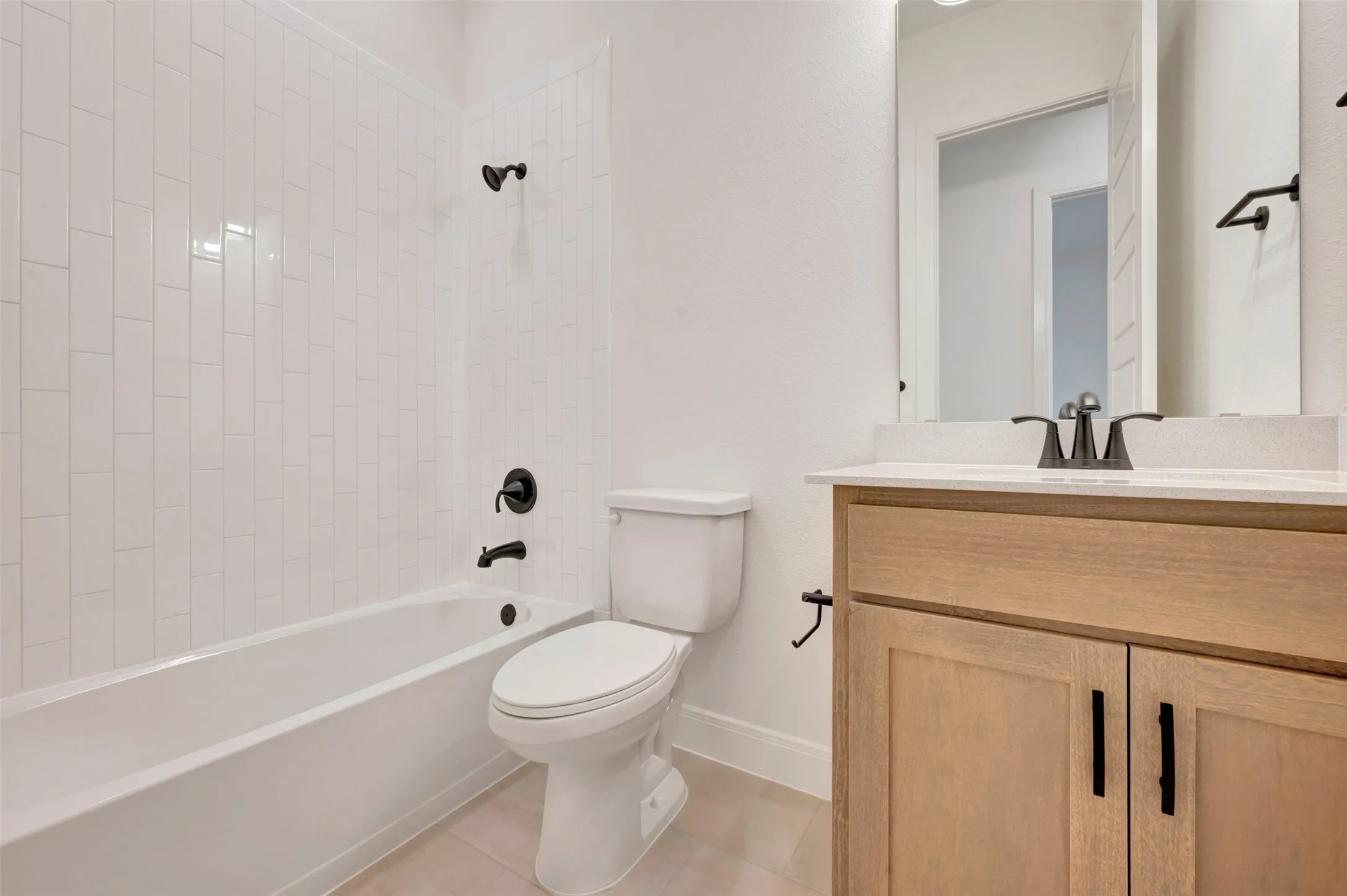 Modern bathroom featuring a white bathtub with subway tile surround, matte black fixtures, a white toilet, and a light wood-finish vanity with a light-colored countertop