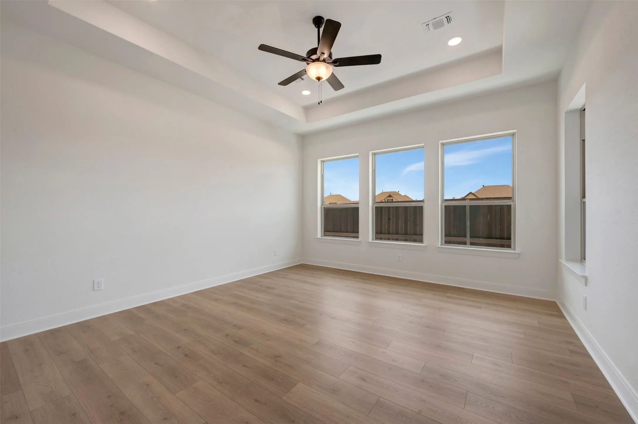 Spacious room featuring wood-finish flooring and a tray ceiling with recessed lighting
