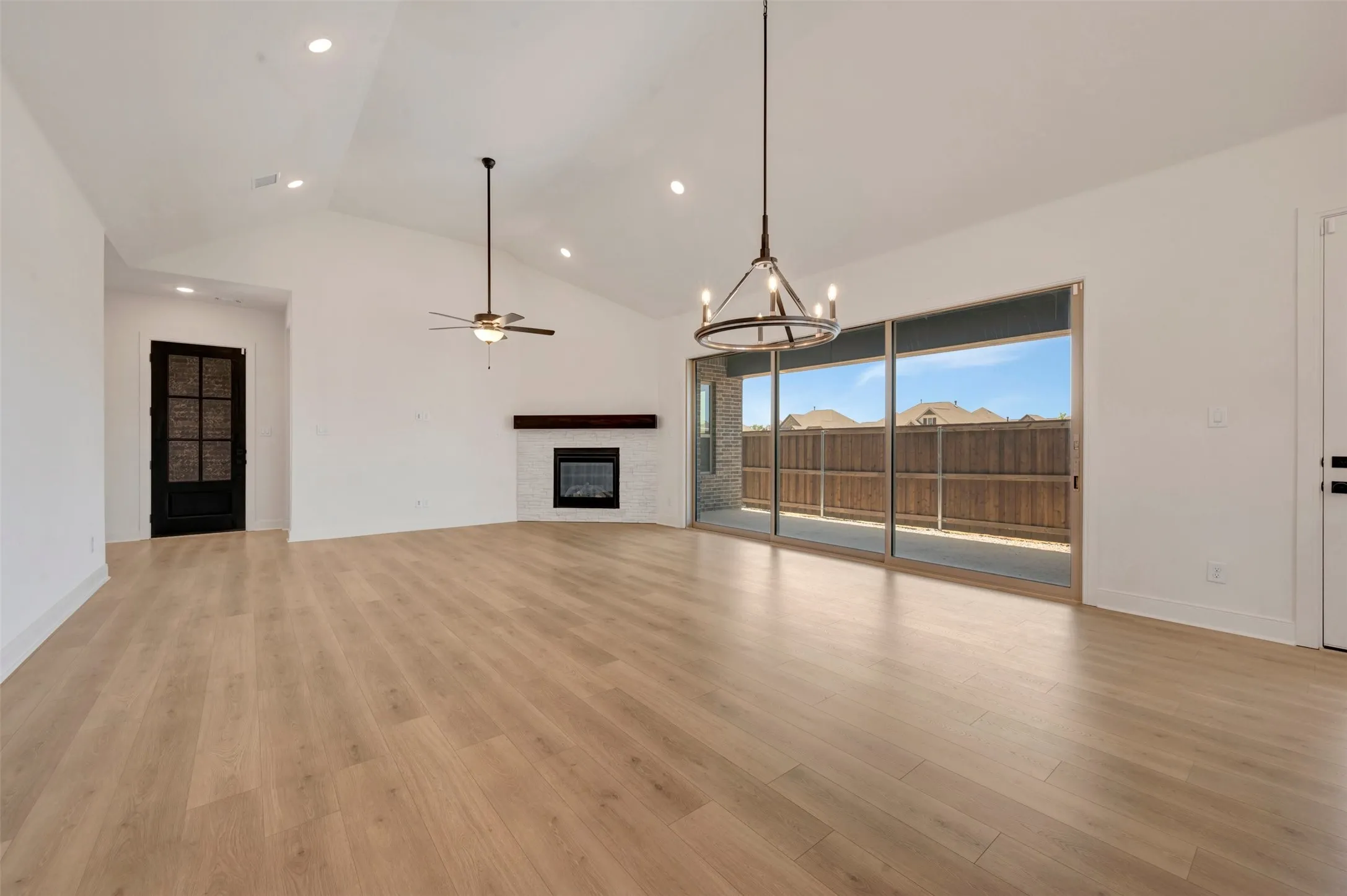 Spacious room featuring vaulted ceilings, wood-finish flooring, and a fireplace with a white tile surround and dark wood mantel