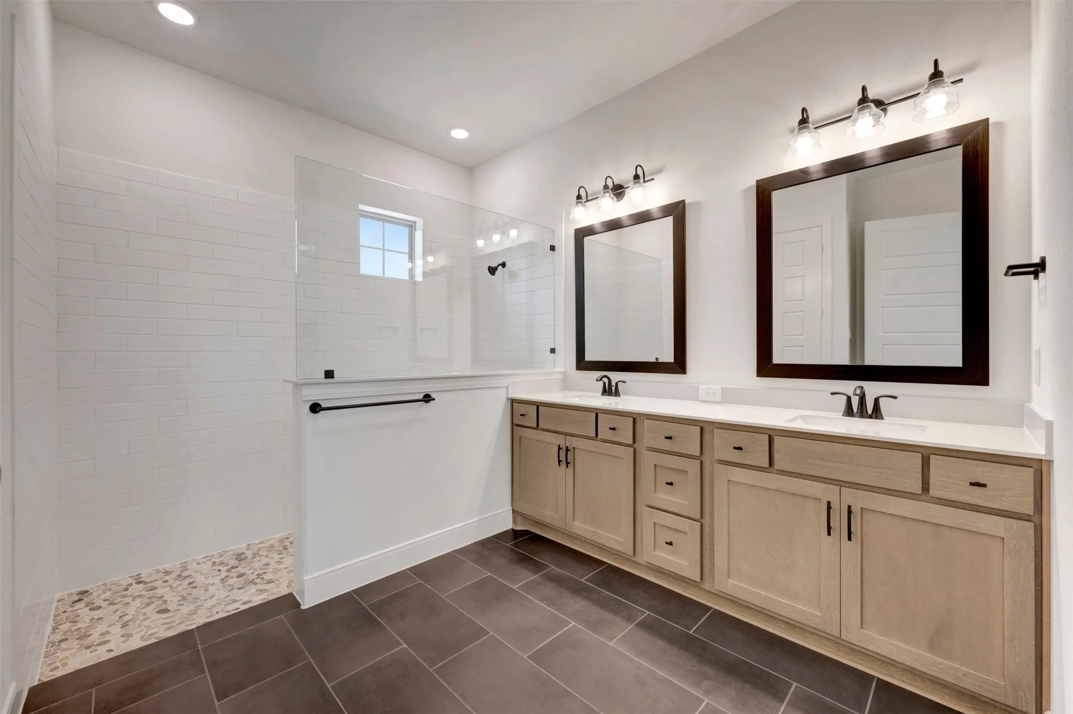 Double vanity with light wood-finish cabinetry, white countertops, and dual framed mirrors