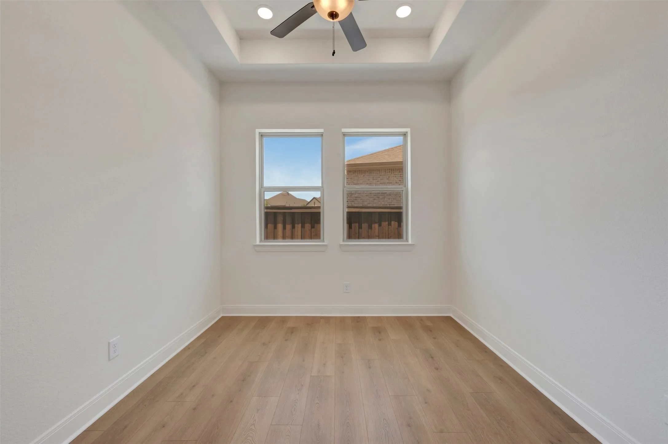Room featuring wood-finish flooring and a tray ceiling with a ceiling fan