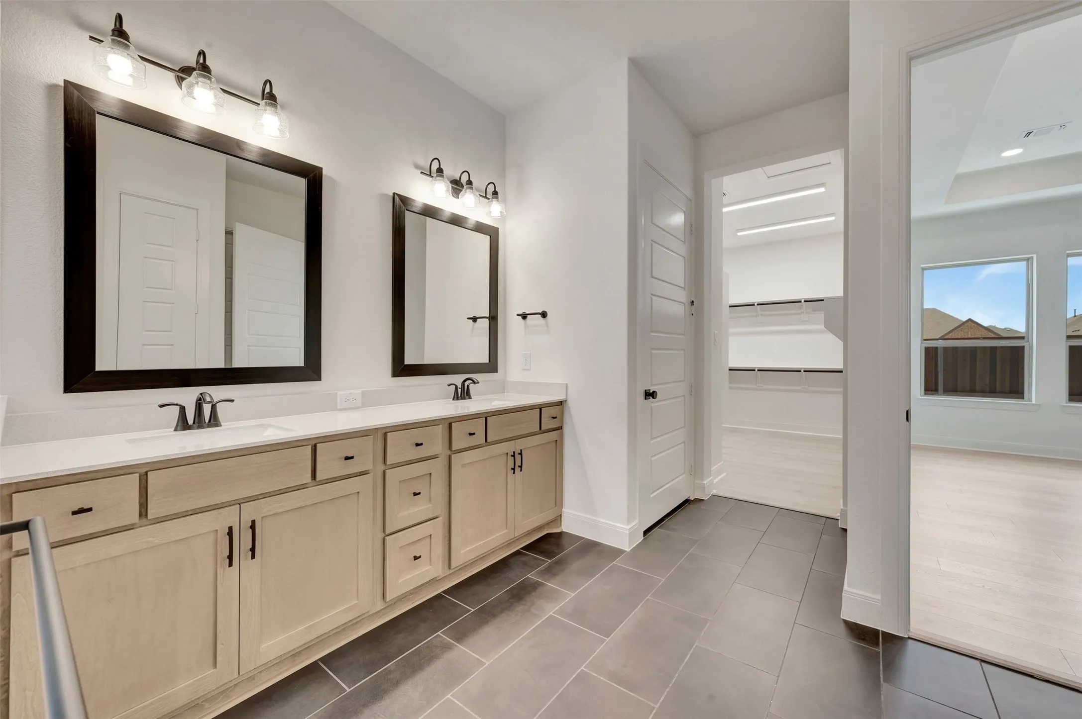 Dual vanity with light wood-finish cabinetry, white countertops, and dark framed mirrors