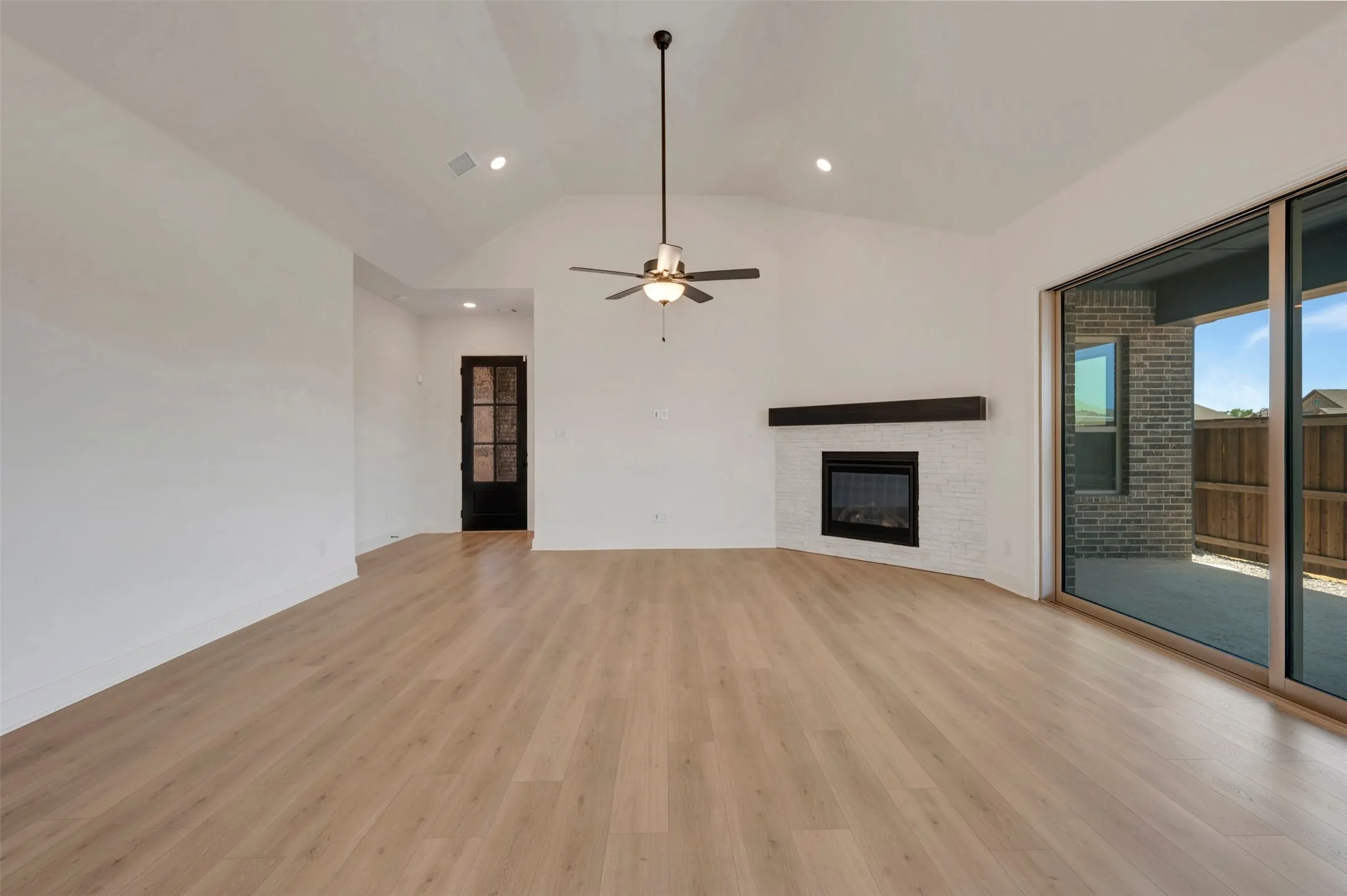 Vaulted ceiling room featuring wood-finish flooring, a white brick fireplace with dark wood mantel, and sliding glass doors to a patio