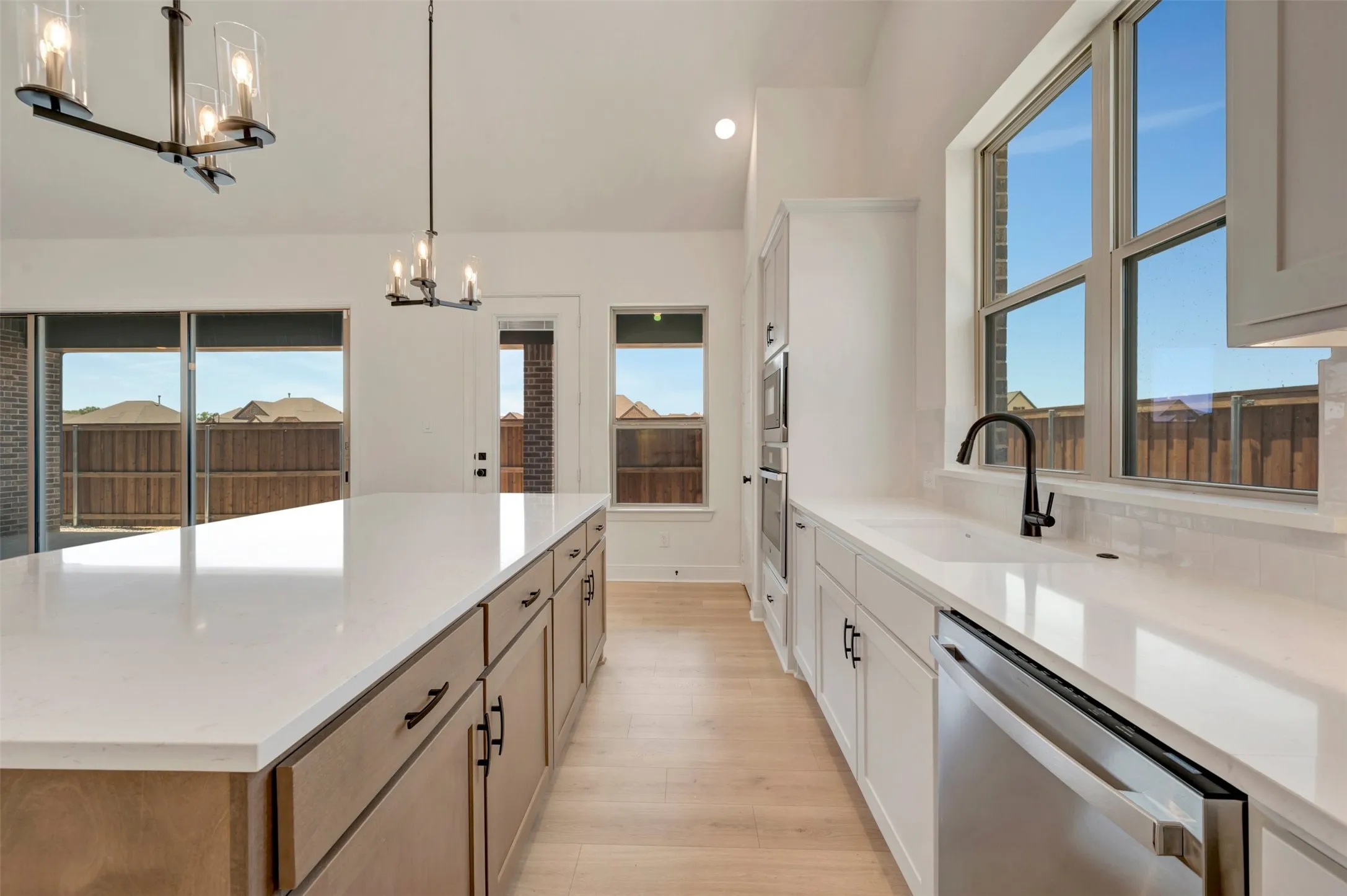 Modern kitchen featuring an expansive island with a light-toned countertop, light wood-finish flooring, white cabinetry, stainless steel appliances, and a black gooseneck faucet