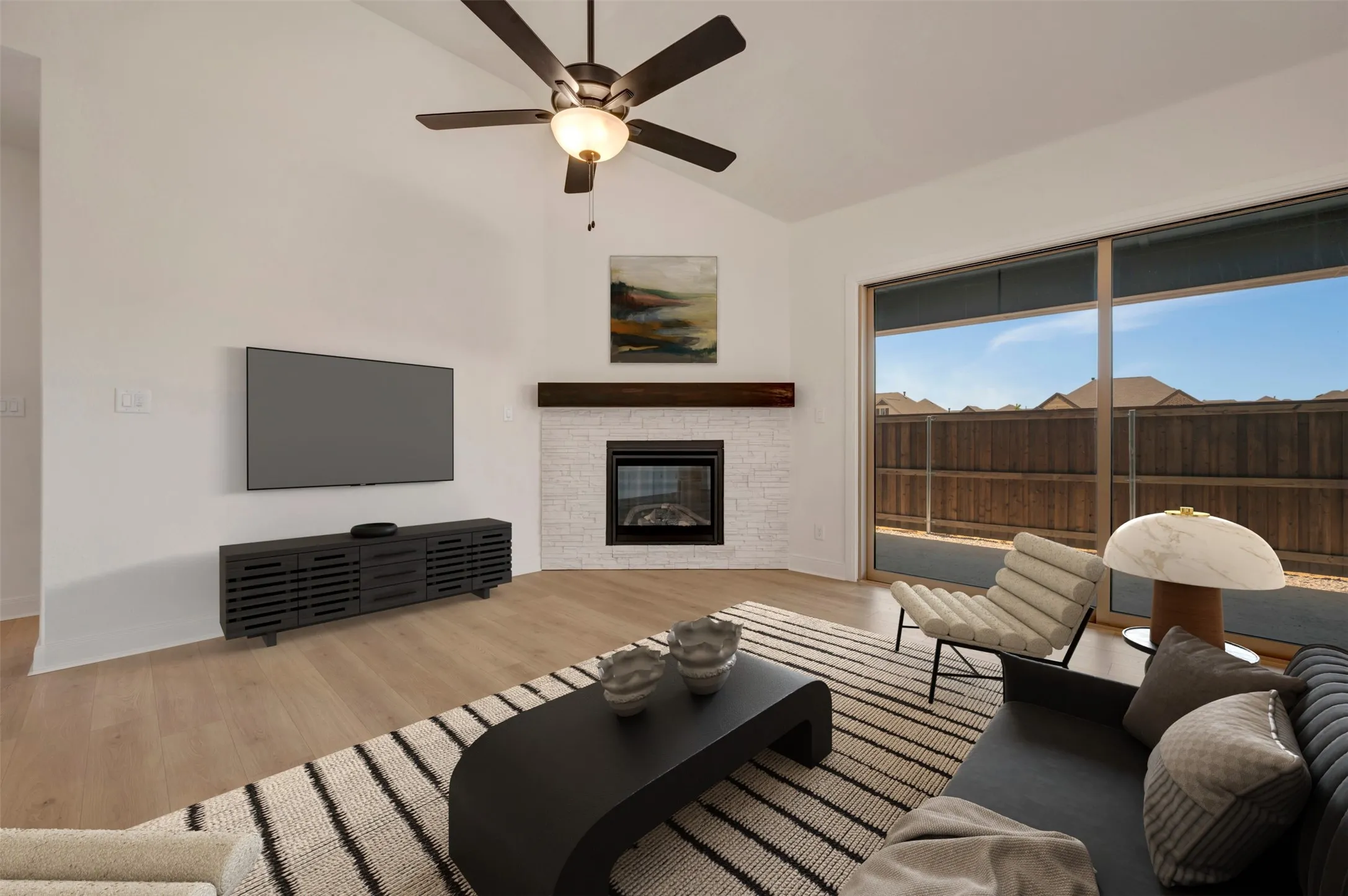 Living area featuring a vaulted ceiling with a ceiling fan, light wood-finish flooring, and a fireplace with a white brick surround and wood mantle
