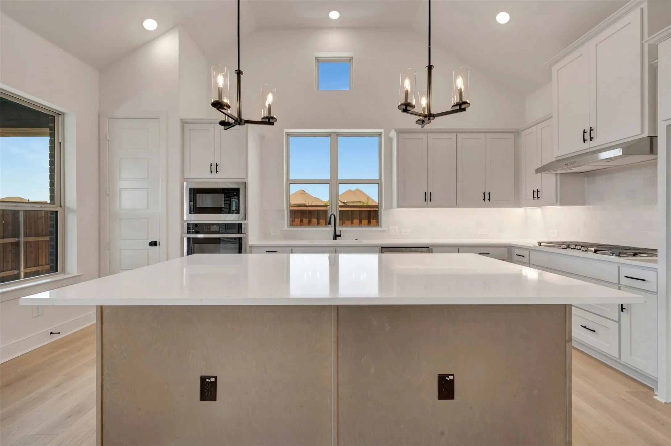 Spacious kitchen featuring a large central island with a light-toned base, white countertop, and integrated outlets