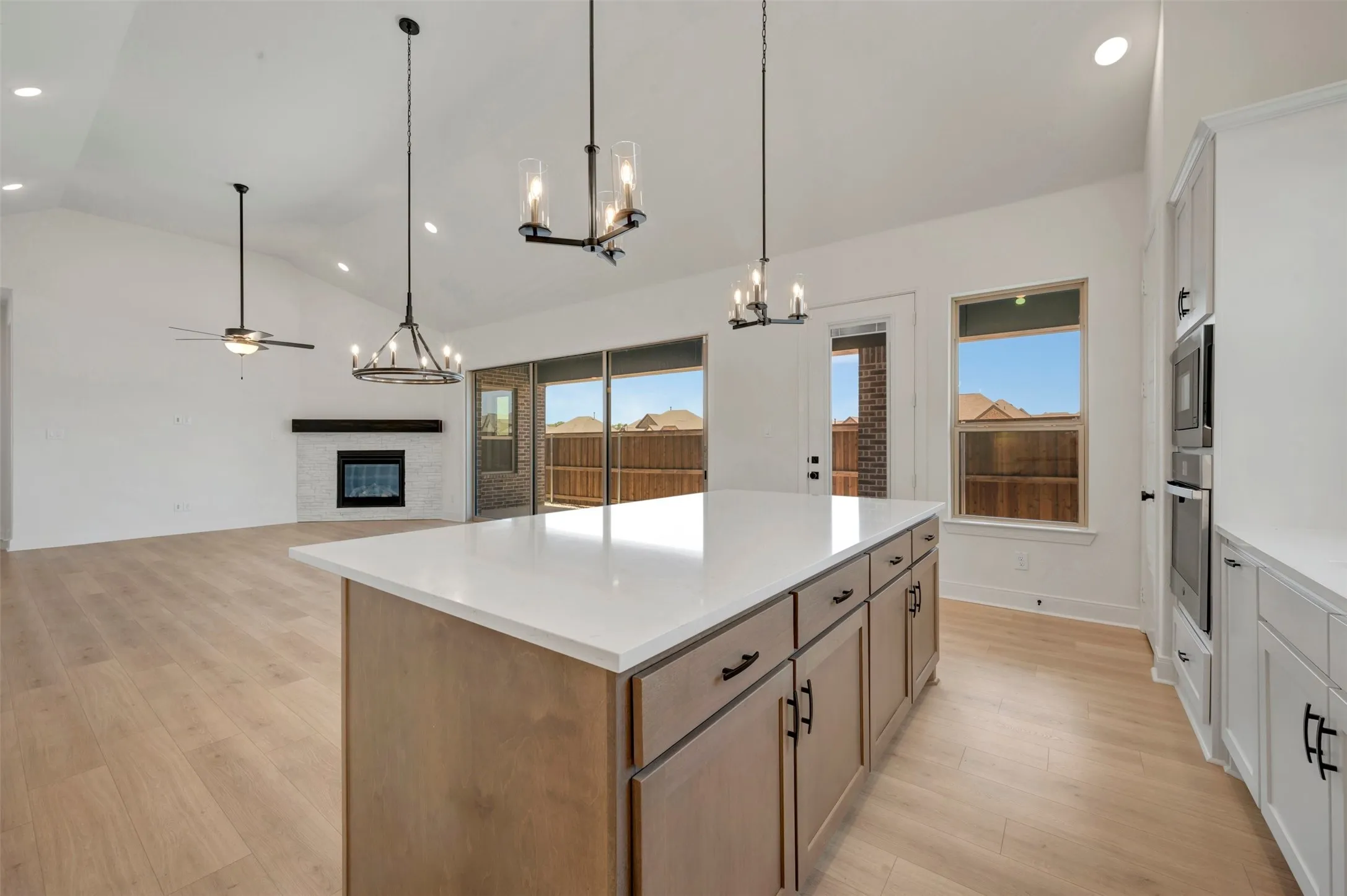 Expansive open-concept living area featuring a kitchen island with a light-toned countertop, wood-finish flooring, and vaulted ceilings with recessed lighting