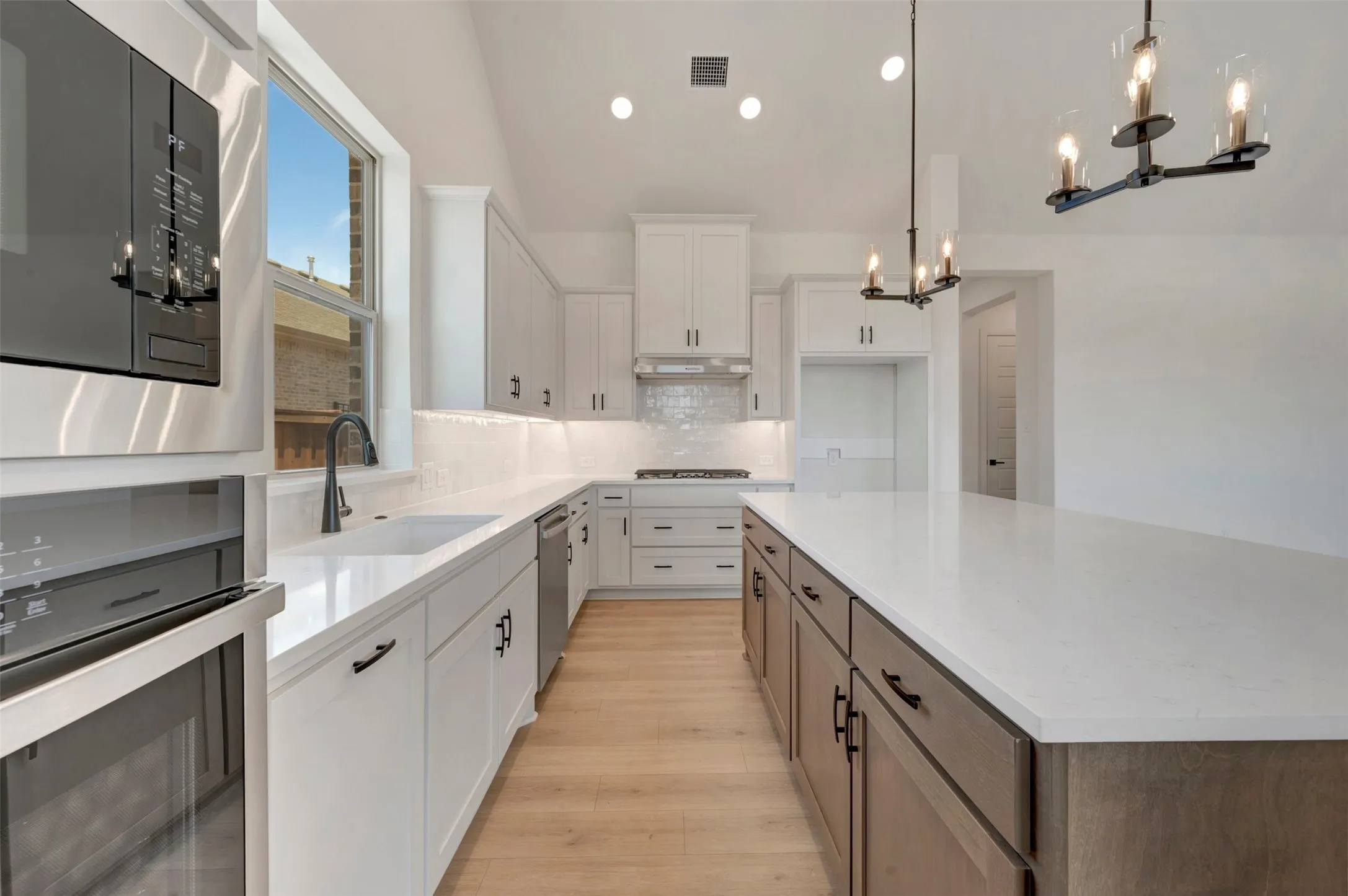 Gourmet kitchen featuring a substantial island with stone countertops, white cabinetry, integrated stainless steel appliances, a tile backsplash, and wood-finish flooring