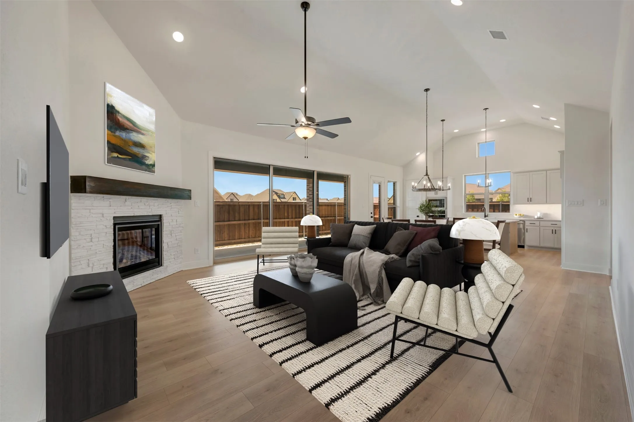 Open-concept living area featuring vaulted ceilings, wood-finish flooring, a white brick fireplace with a dark wood mantel, recessed lighting, and sliding glass doors