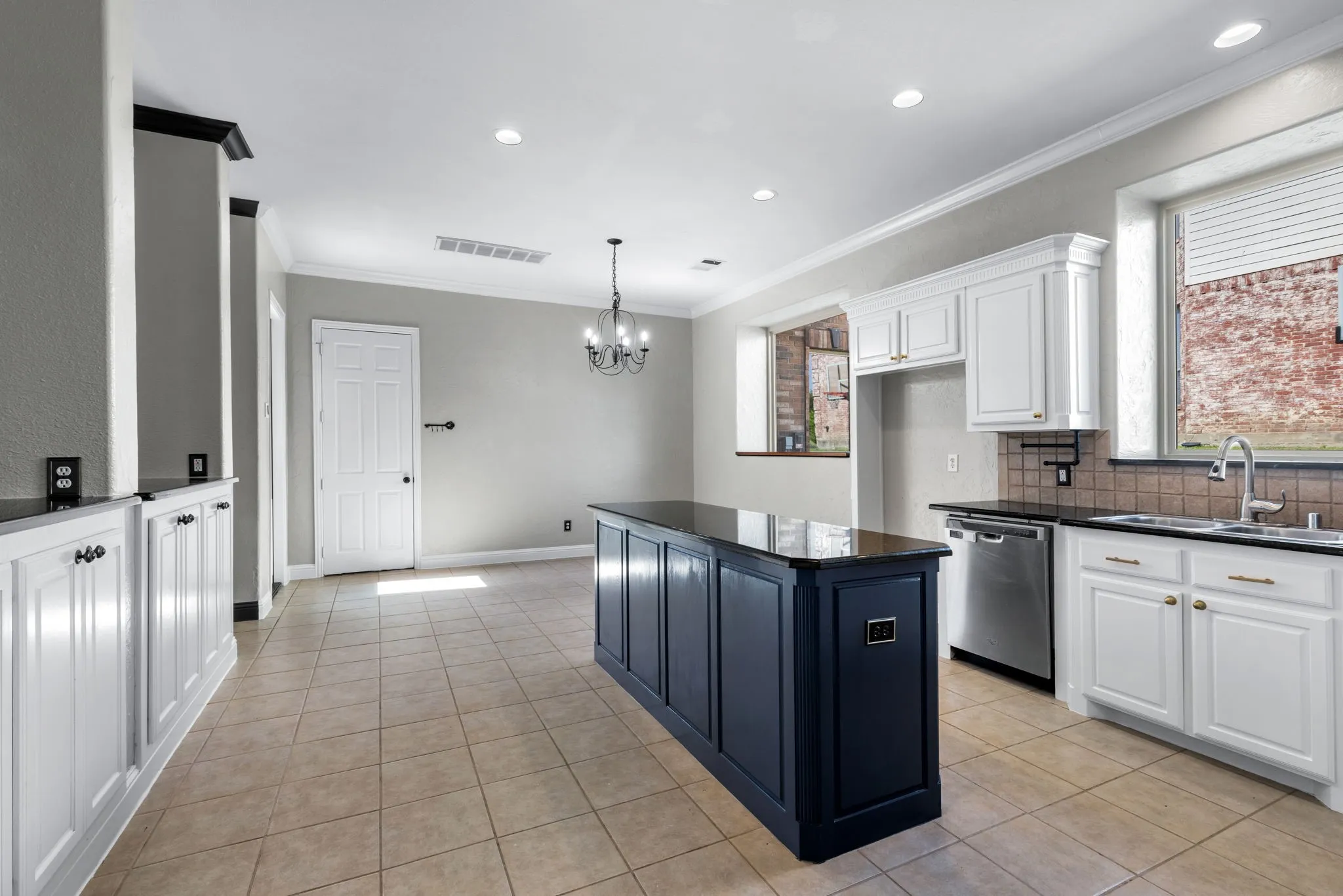 Kitchen featuring a navy blue island with a dark countertop, white perimeter cabinetry, stainless steel dishwasher, and a tile backsplash
