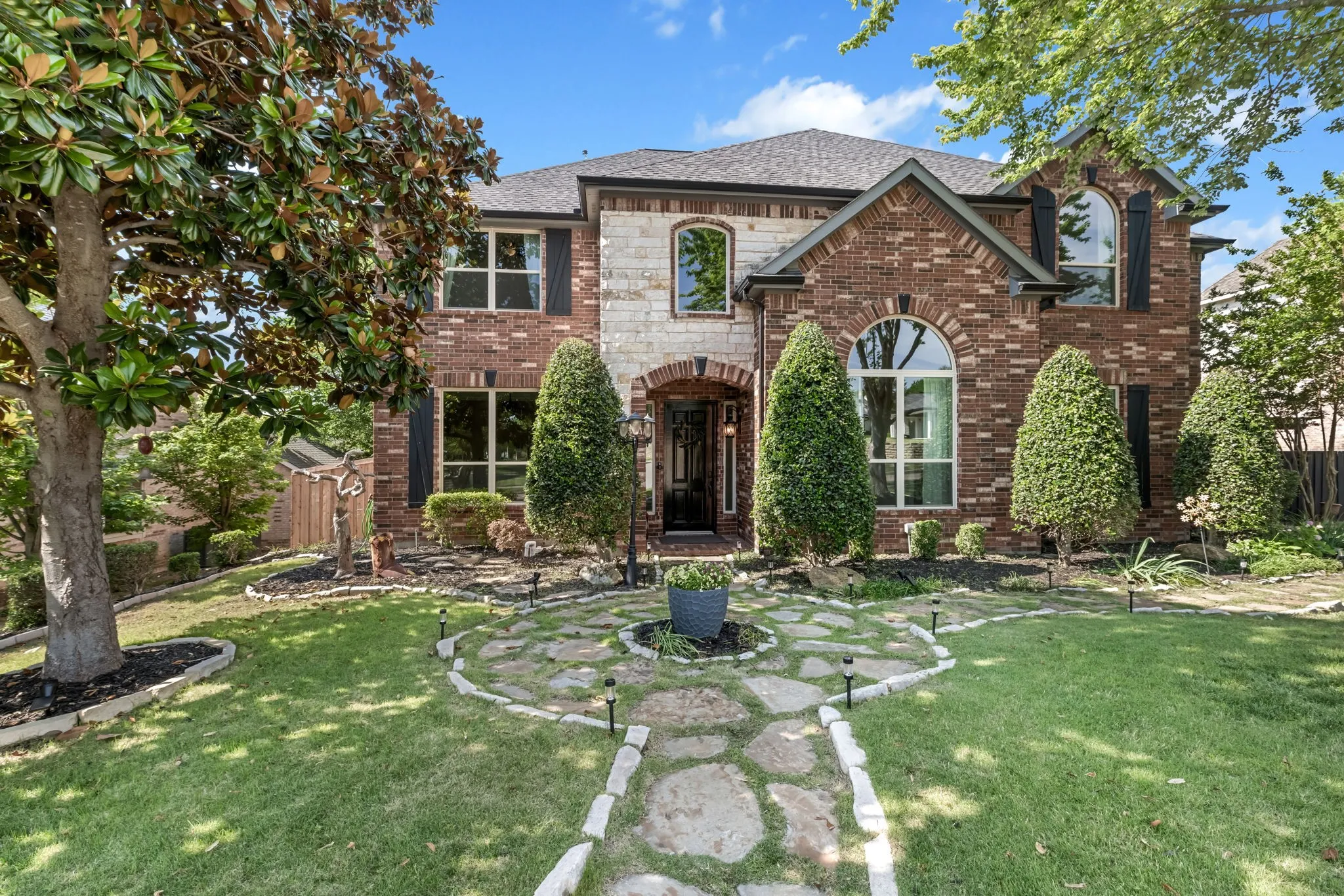 Traditional two-story exterior featuring a brick and stone facade, arched entryway, and dark shutters