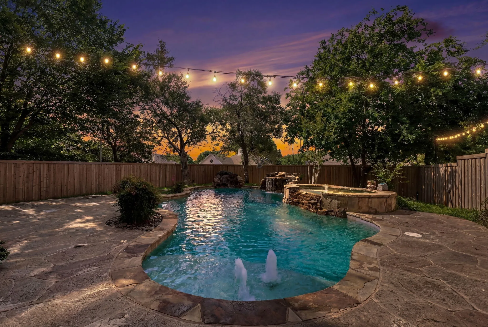 Resort-style backyard featuring a freeform swimming pool with stone coping, integrated spa with waterfall, and stamped concrete  patio