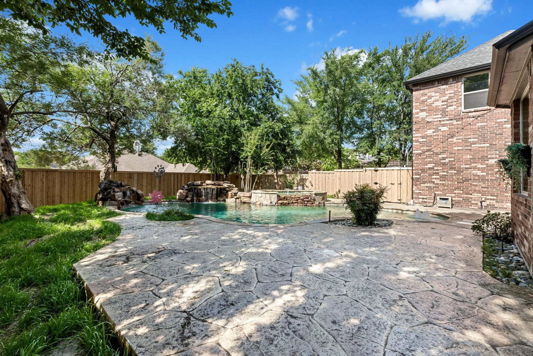 Private backyard oasis featuring a stamped concrete patio, a custom swimming pool with rock waterfalls, and a raised spa