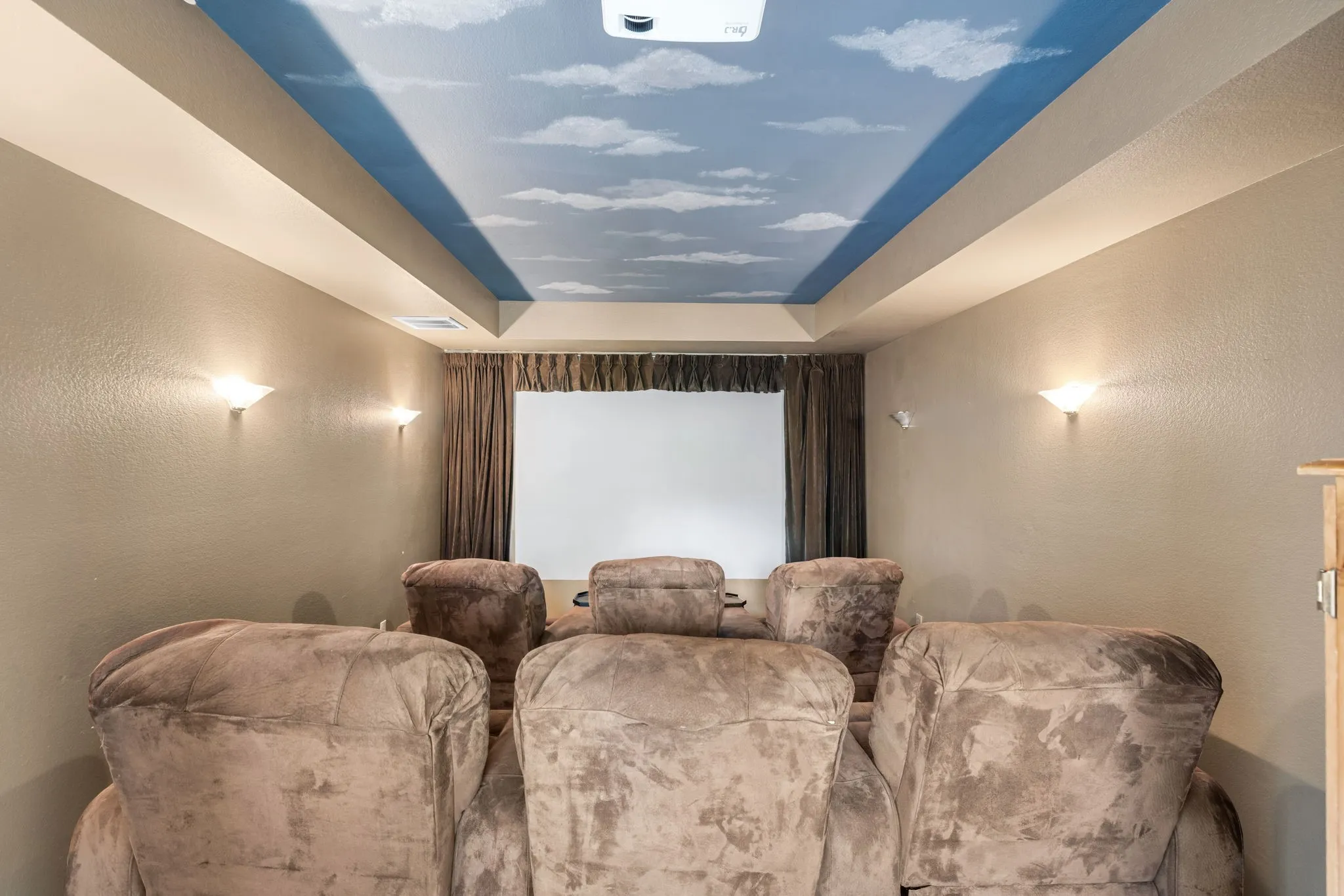 Dedicated media room featuring a large projection screen, wall-mounted sconces, and a painted sky-themed ceiling