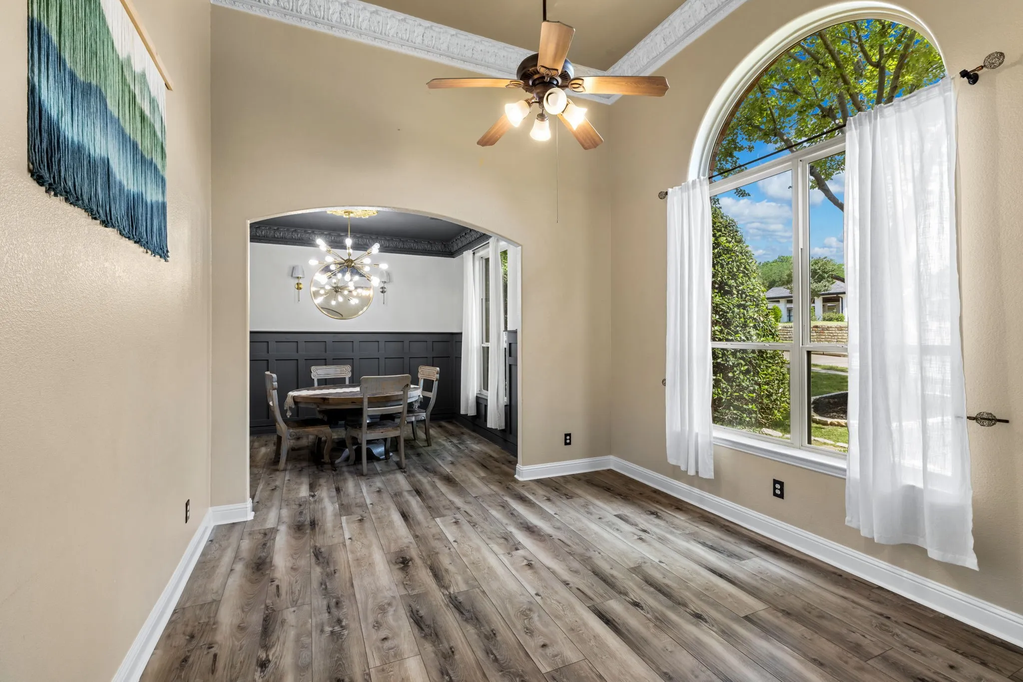 Room featuring wood-finish flooring, an arched window with an upper transom, and a ceiling fan